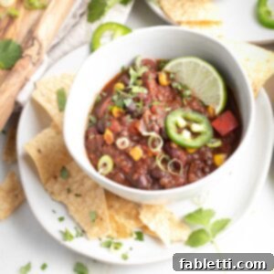 Quick and Flavorful Vegan Lentil Chili 12 A generous bowl of vegan chili, brimming with lentils, red peppers, and corn, beautifully garnished with fresh lime, cilantro, and jalapeño slices.