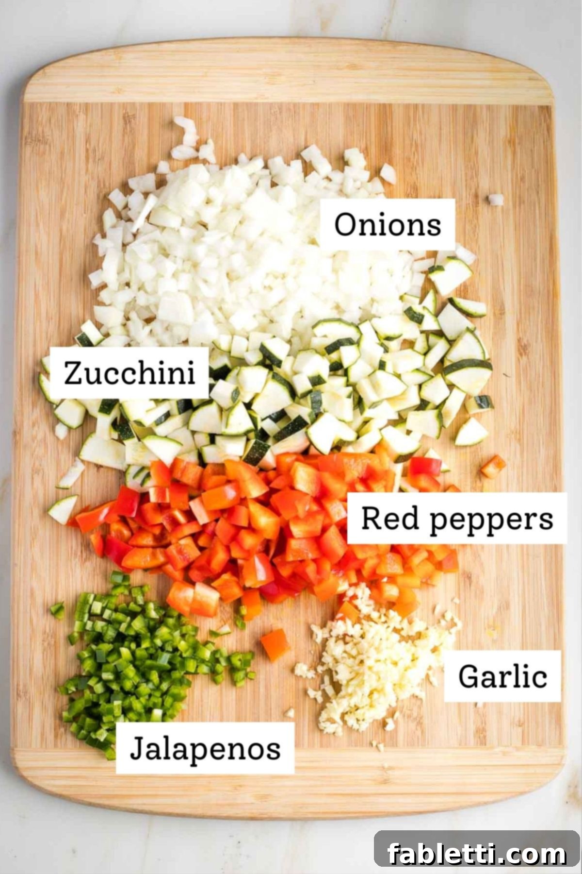 Quick and Flavorful Vegan Lentil Chili 5 A cutting board filled with an assortment of freshly diced and minced vegetables ready for chili preparation: yellow onions, green zucchini, vibrant red bell peppers, sliced jalapeños, and finely minced garlic.