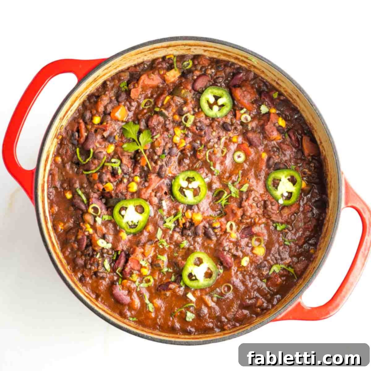 Quick and Flavorful Vegan Lentil Chili 10 A large Dutch oven brimming with thick, homemade vegan lentil chili, beautifully topped with fresh cilantro sprigs and vibrant jalapeño slices, ready to be served.