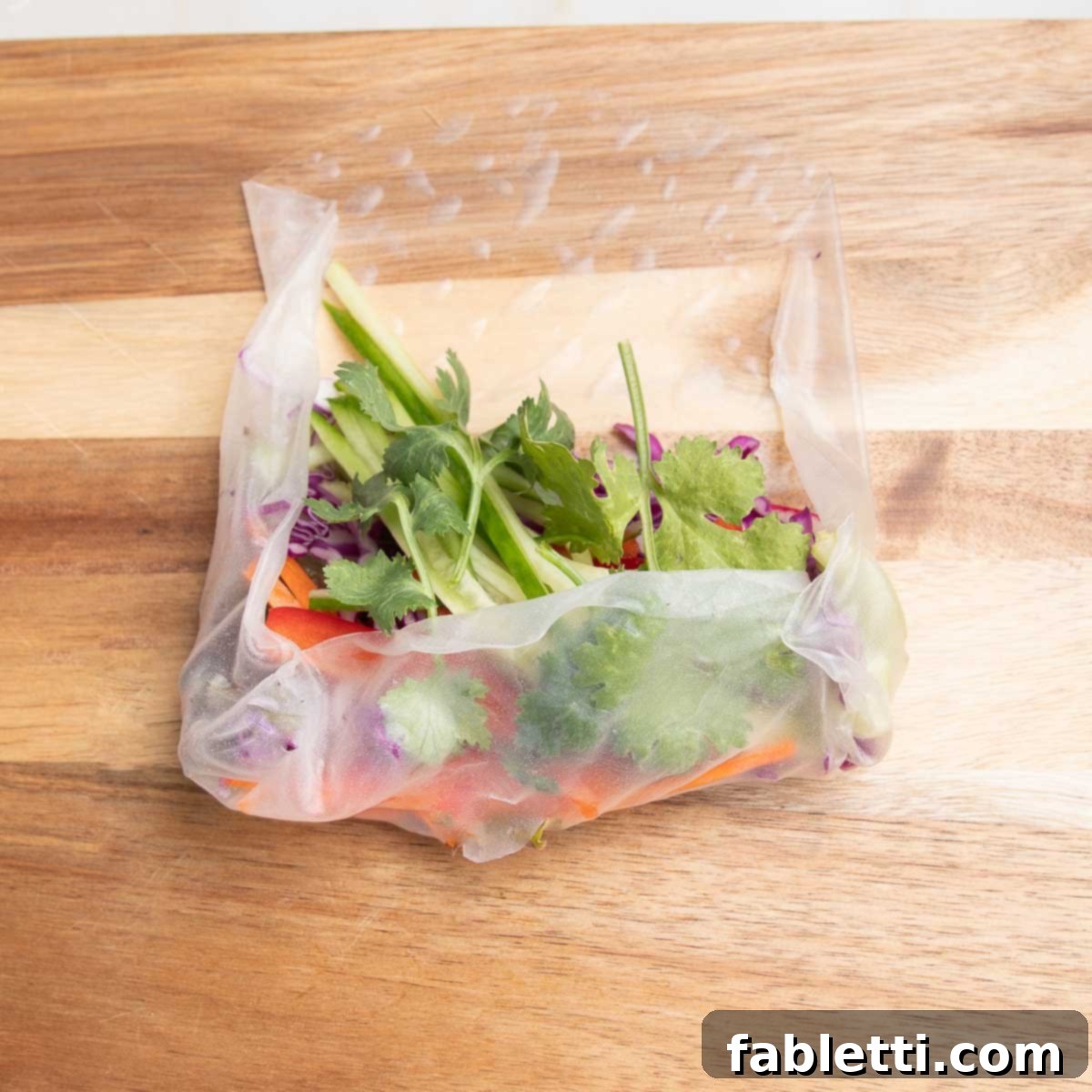 The rolling process of a fresh spring roll, with the bottom and both side edges now folded inwards over the colorful vegetable pile.