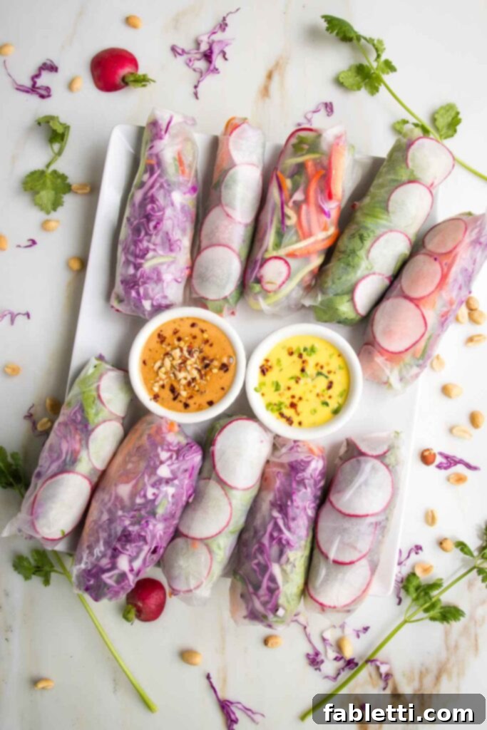 A large rectangular platter brimming with an assortment of colorful fresh spring rolls, accompanied by two vibrant dipping sauces: a yellow mango dressing and an orange-hued peanut butter sauce.