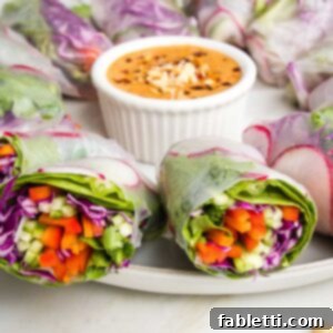 Fresh spring rolls cut in half with colorful julienned veggies shown and a small dish of peanut sauce. veggies