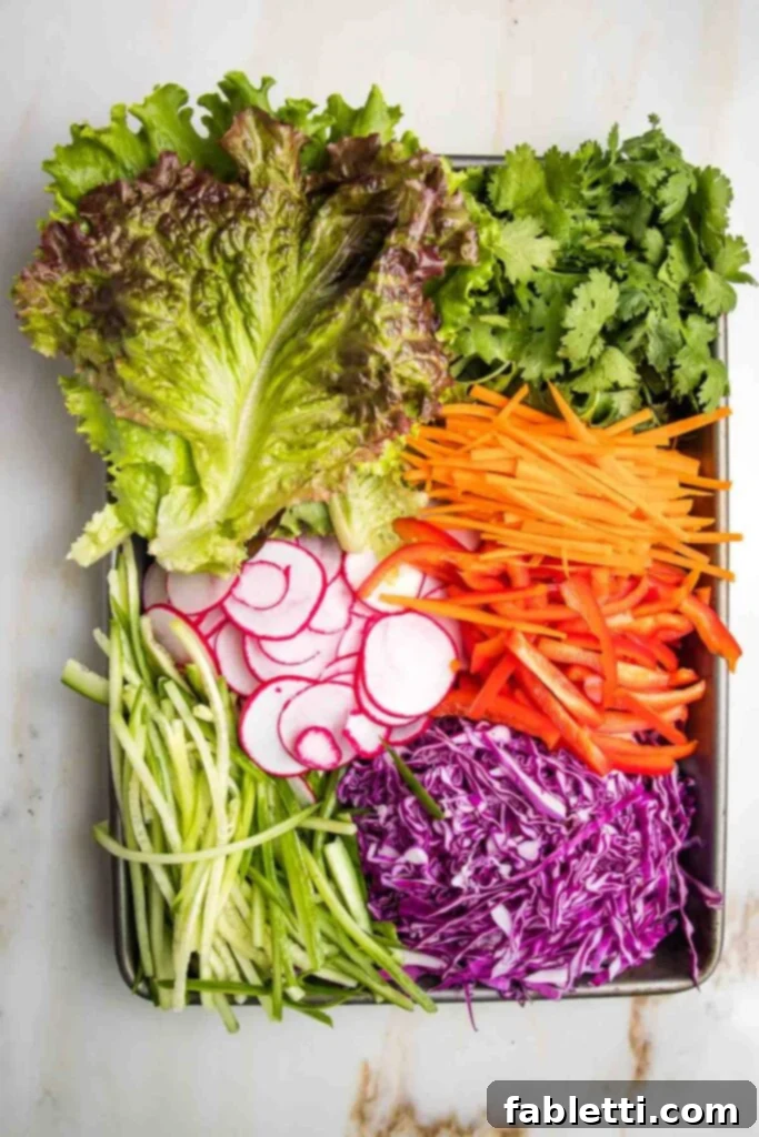A tray filled with neatly prepped spring roll ingredients including fresh lettuce leaves, cilantro, thinly sliced radish, shredded purple cabbage, julienned carrots, red bell peppers, and cucumbers.