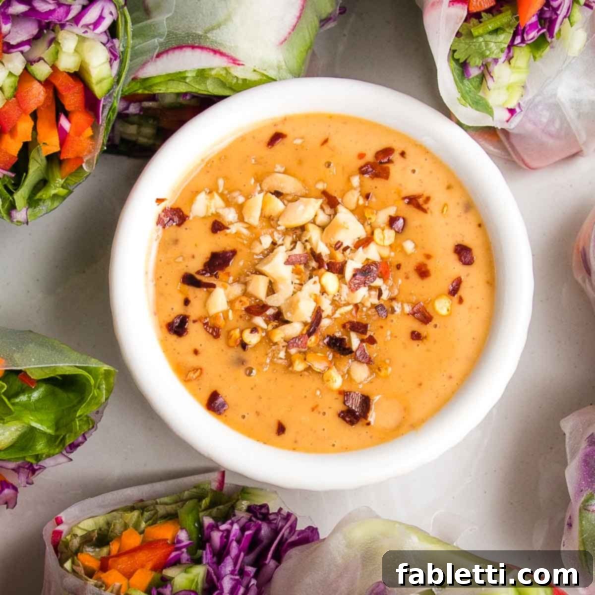 Close-up view of a bowl of homemade peanut sauce for spring rolls, garnished with crushed peanuts and a scattering of red pepper flakes.