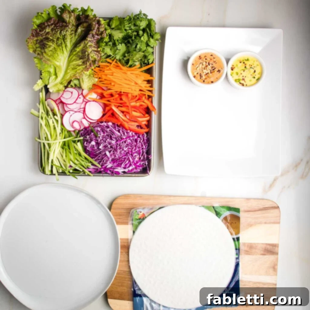Overhead view of a prepared spring roll assembly station, featuring a shallow dish of water for wrappers and various chopped vegetables.