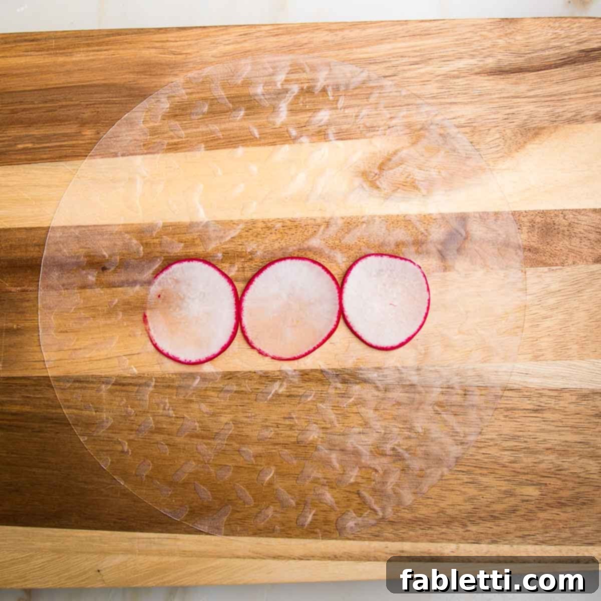 A softened rice paper wrapper laid on a cutting board, with three thinly sliced radishes placed near the bottom edge.
