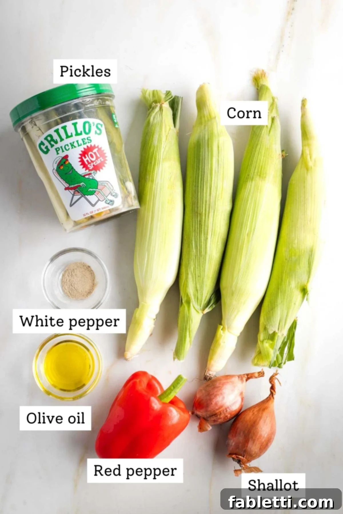 Zesty Israeli Corn and Pickle Salad 3 Labeled ingredients for Israeli Corn Salad: pickles, corn kernels, white pepper, olive oil, diced red bell pepper, and chopped shallots, arranged neatly.