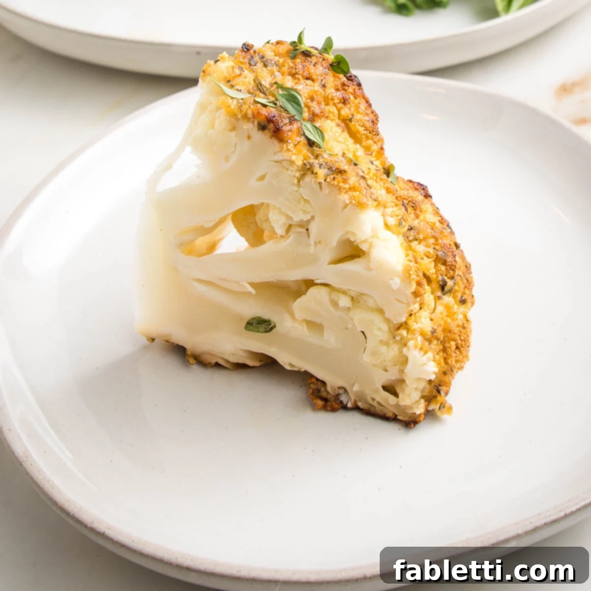 A wedge of a whole roasted cauliflower on a white plate. Golden on the outside, tender on the inside.