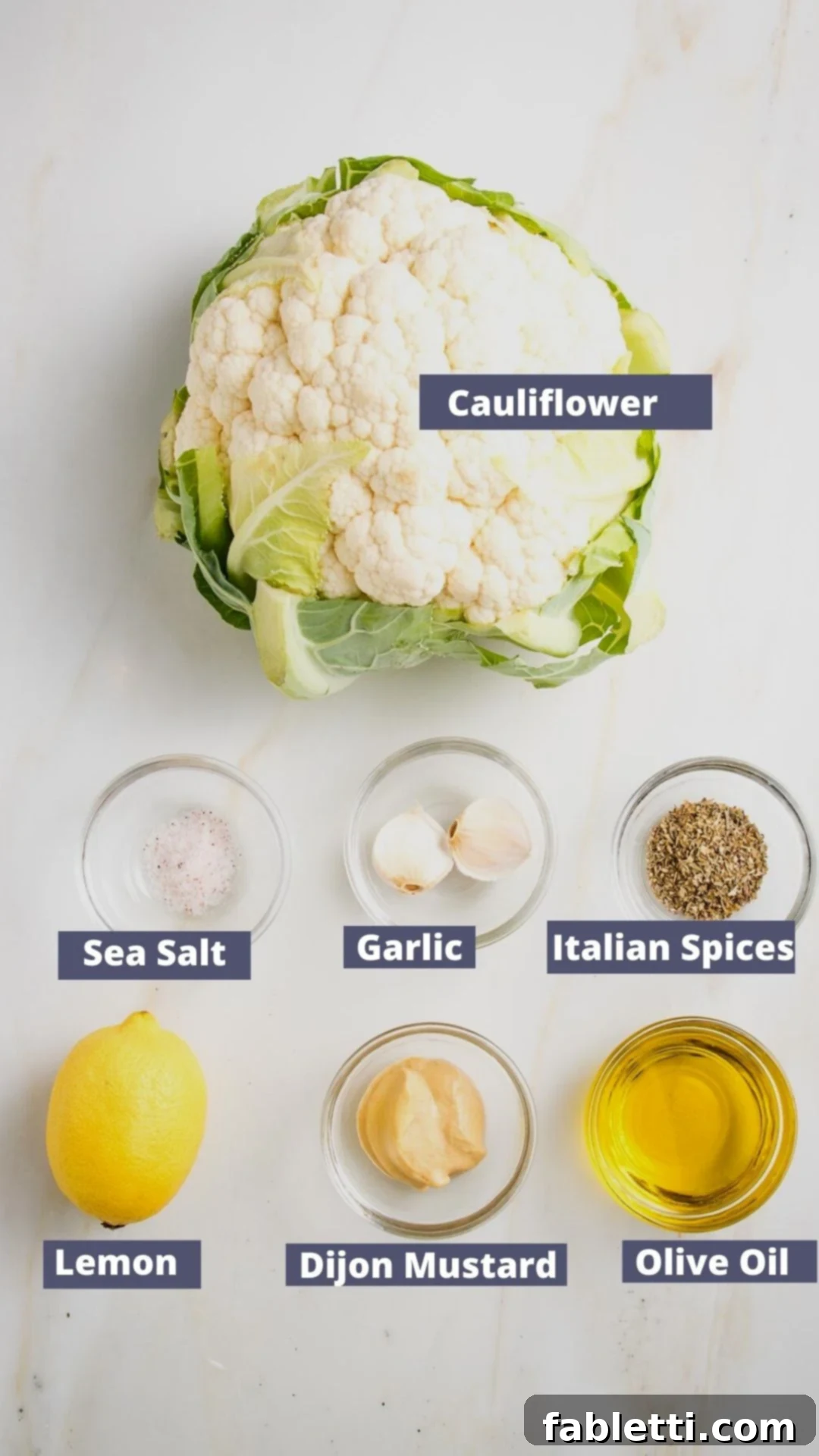 Labeled ingredients for whole roasted cauliflower: cauliflower, olive oil, mustard, lemon, sea salt, garlic cloves and italian spices.