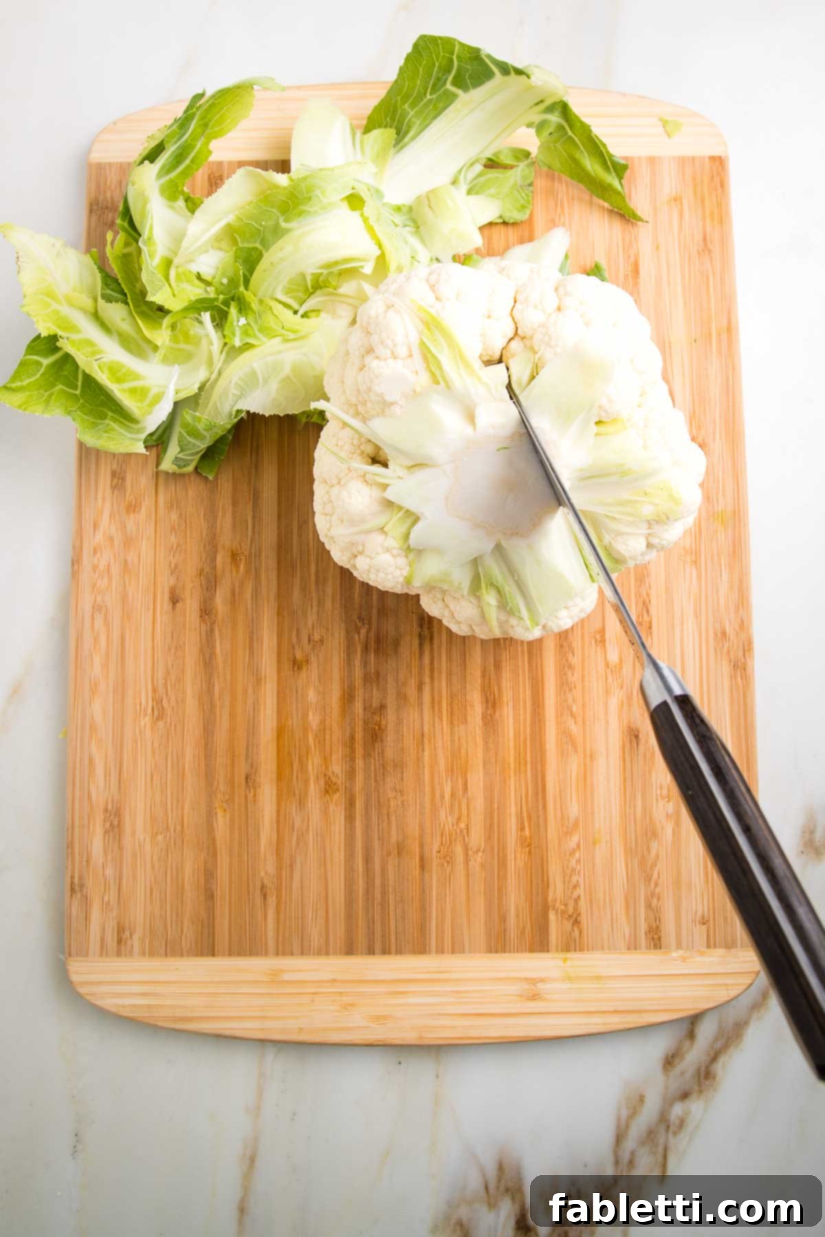 Head of cauliflower with knife, trimming the core out of the center.