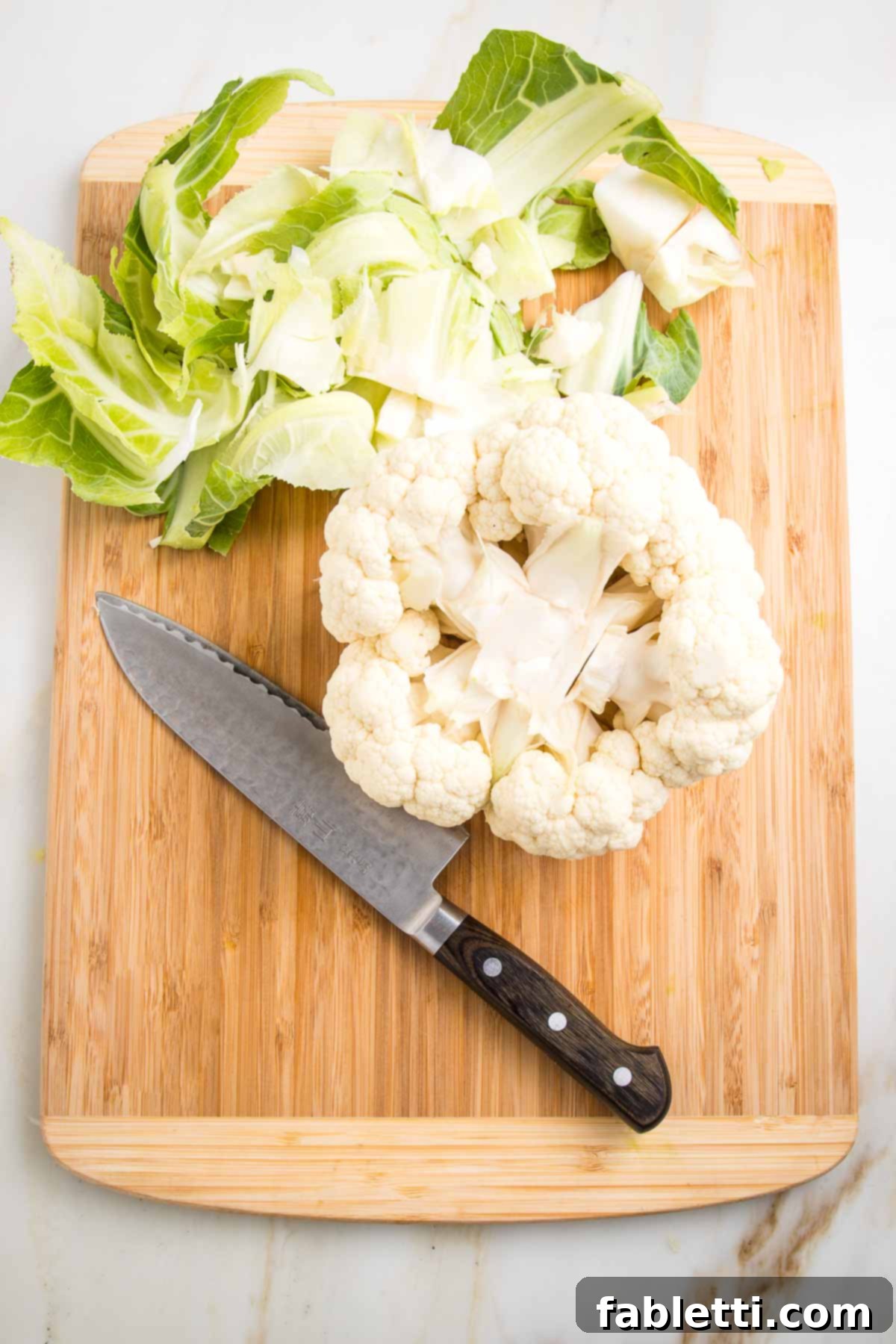 Head of cauliflower turned upside down with the core cut out and the scraps on the side of the cutting board.