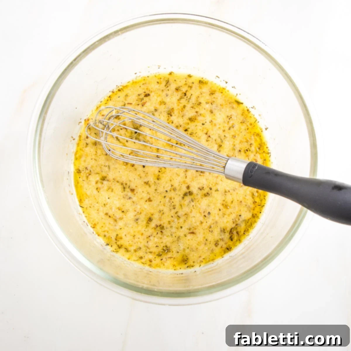Glass bowl with a whisk, and a mustard, lemon herb mixture.