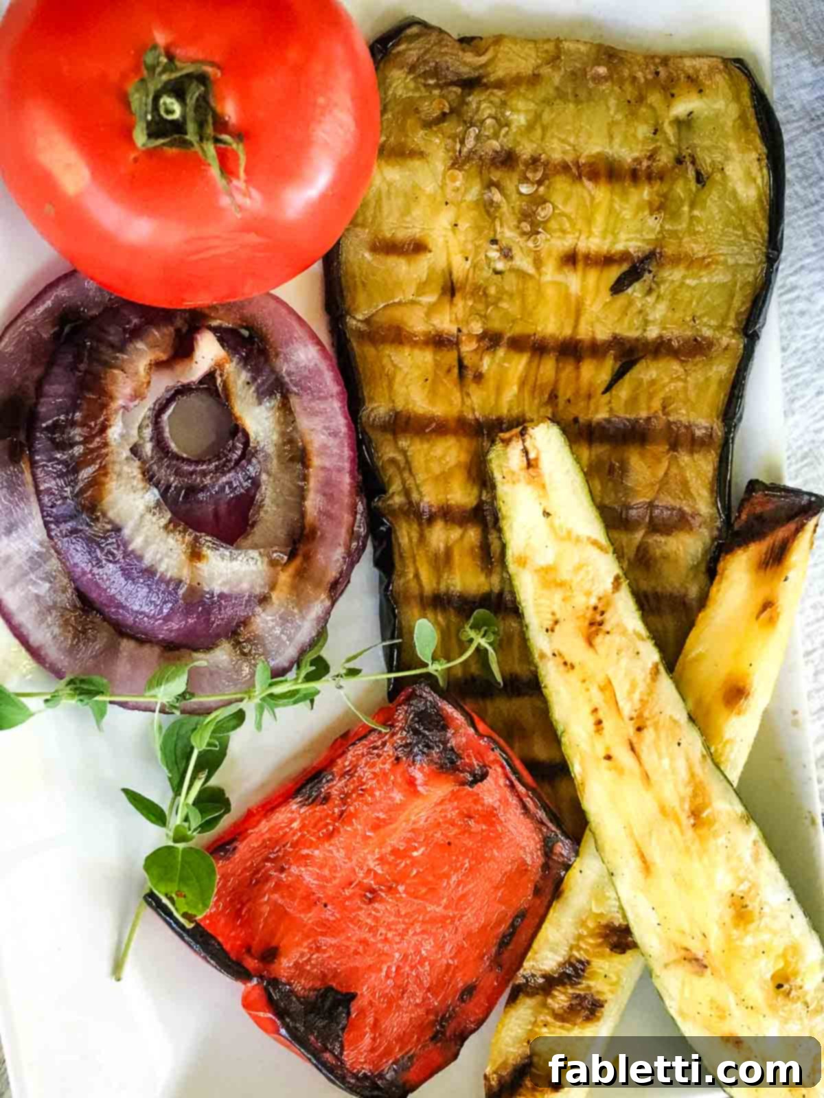 Smoky Grilled Ratatouille Salad 3 Sliced raw eggplant, red onion, red bell pepper, zucchini, yellow squash, and a whole red tomato, arranged before grilling.