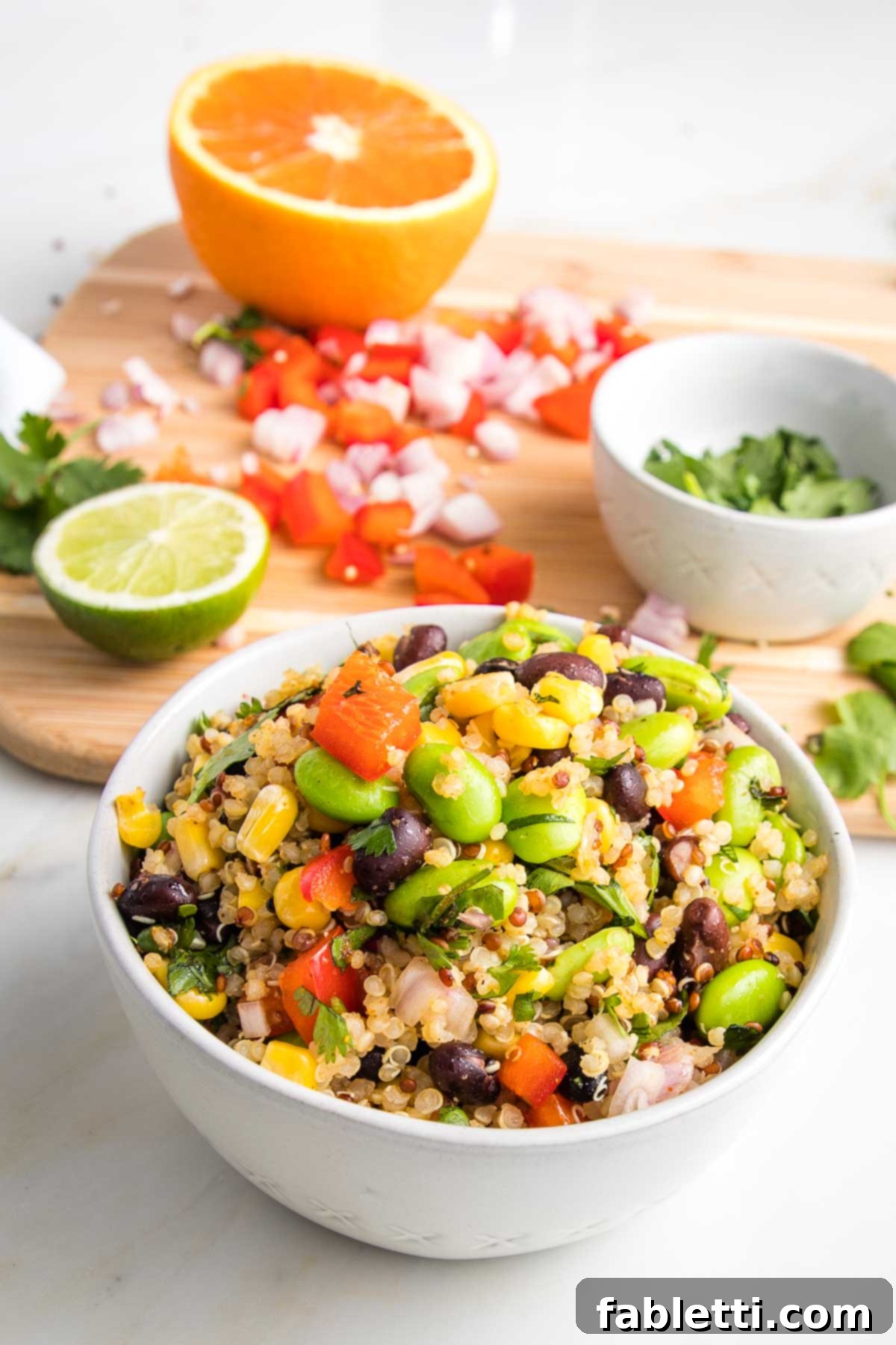 Zesty Southwest Quinoa Salad 9 Bowl of colorful veggies plus quinoa and in the background a cutting board with half an orange, half a lime, chopped red peppers and shallots and cilantro