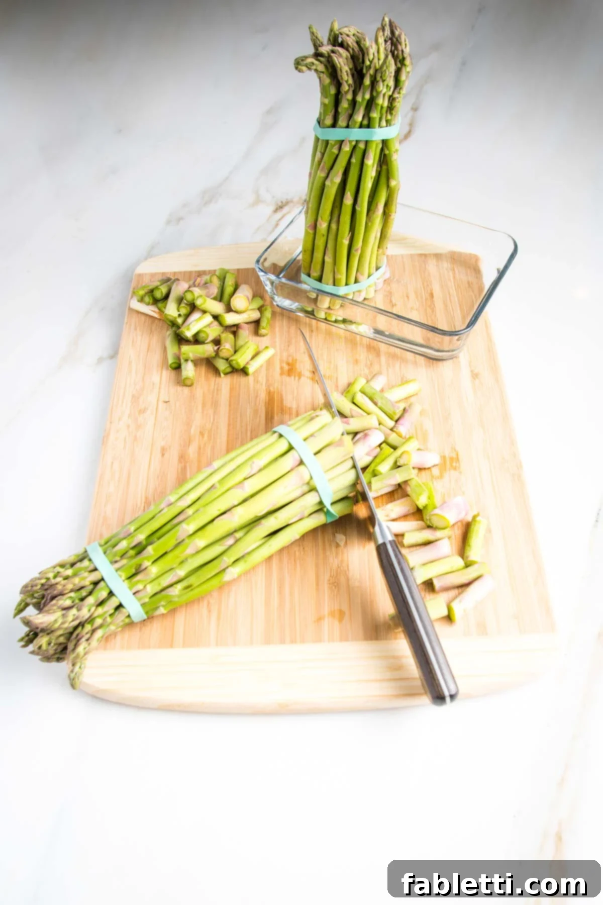 Smoked Asparagus with Dijon Glaze 3 A vibrant green bunch of fresh asparagus spears, bound with a rubber band, stands upright in a shallow dish containing water, illustrating proper storage for extended freshness.