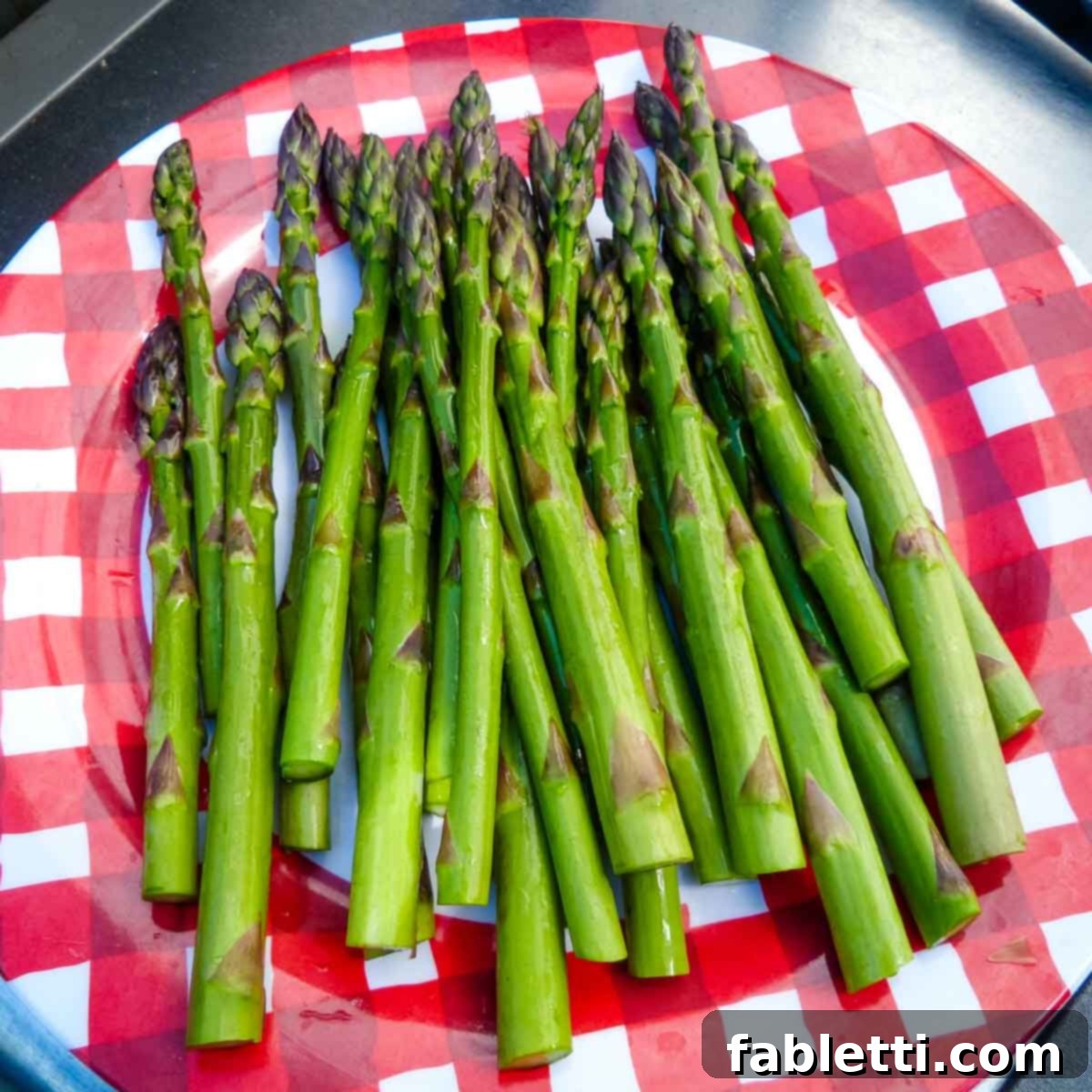Smoked Asparagus with Dijon Glaze 4 Freshly trimmed asparagus spears neatly arranged on a vibrant red checkered plate, highlighting their readiness for grilling.