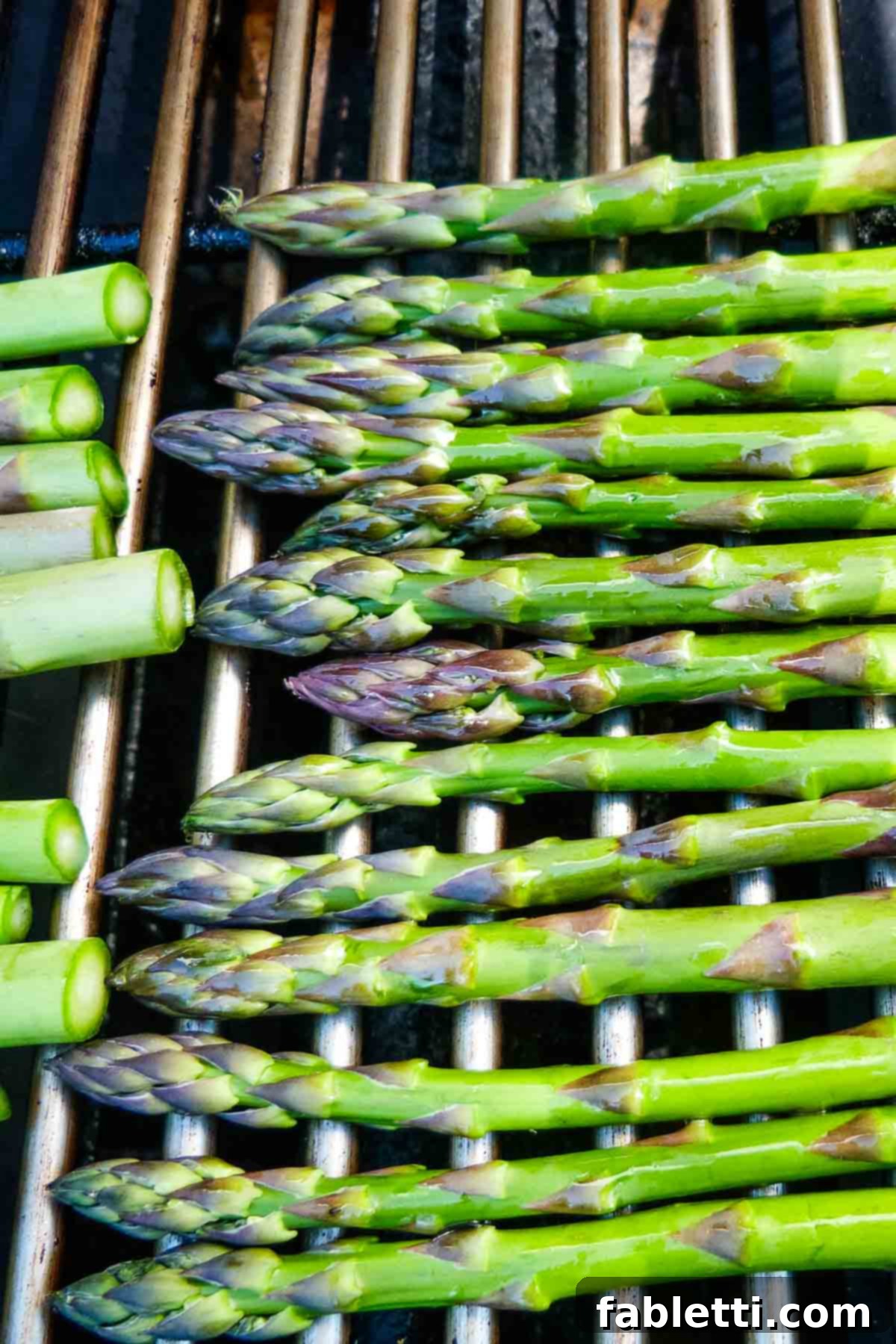 Smoked Asparagus with Dijon Glaze 5 Vibrant green asparagus spears are meticulously laid across the hot grates of a clean grill, showcasing the perfect setup for achieving beautiful char marks.