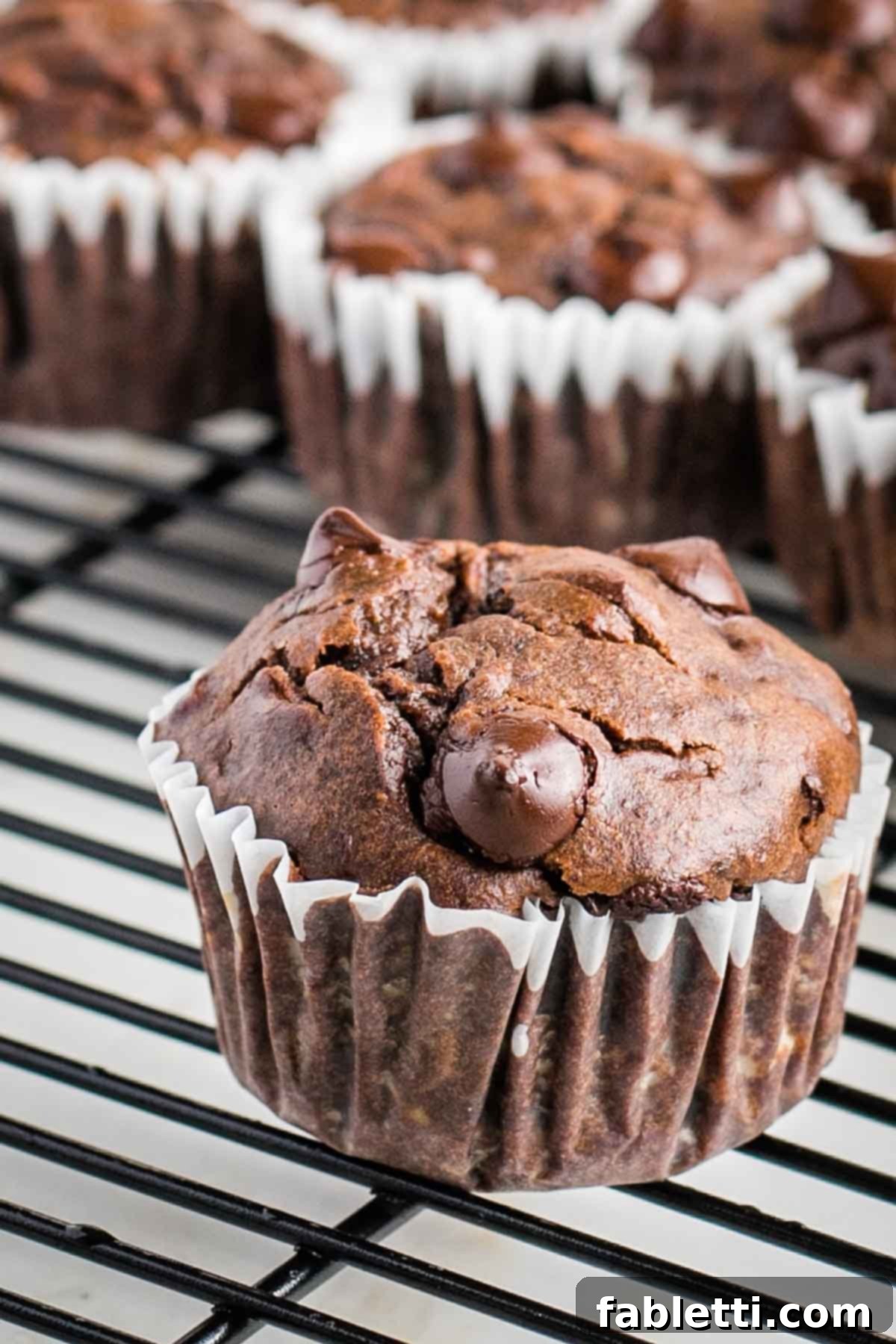 Decadent Double Chocolate Zucchini Muffins 12 Close up of a double chocolate muffin cooling on a wire rack.