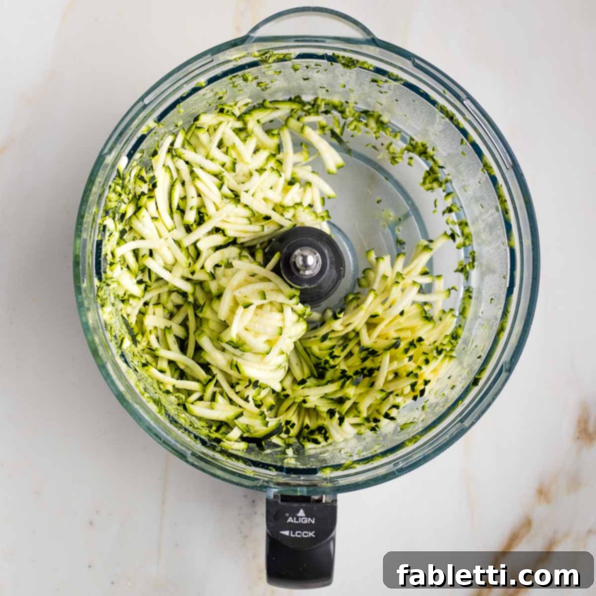 Decadent Double Chocolate Zucchini Muffins 5 Shredded zucchini in the bowl of a food processor.