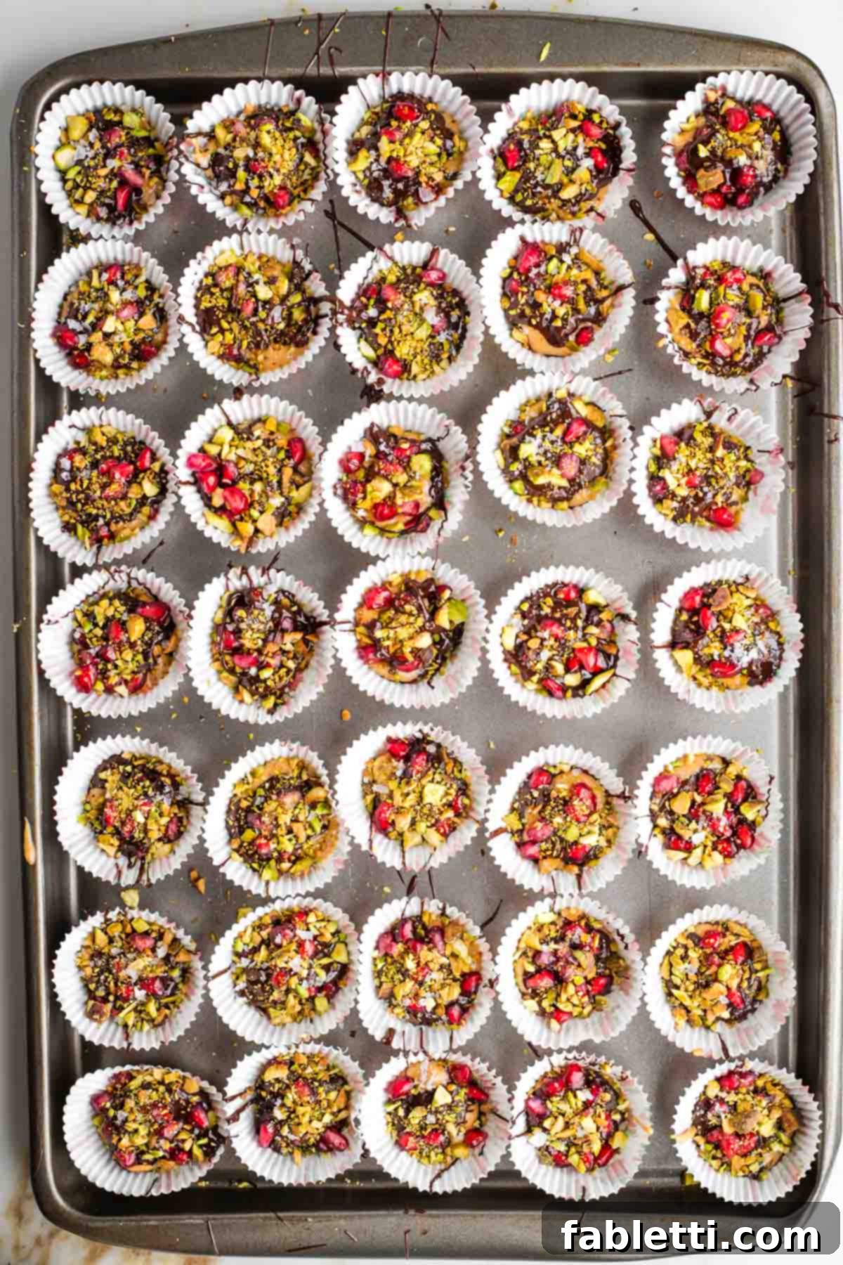 Jeweled Chocolate Peanut Butter Cups 11 A baking tray of set chocolate peanut butter cups, topped with pistachios and pomegranate seeds.