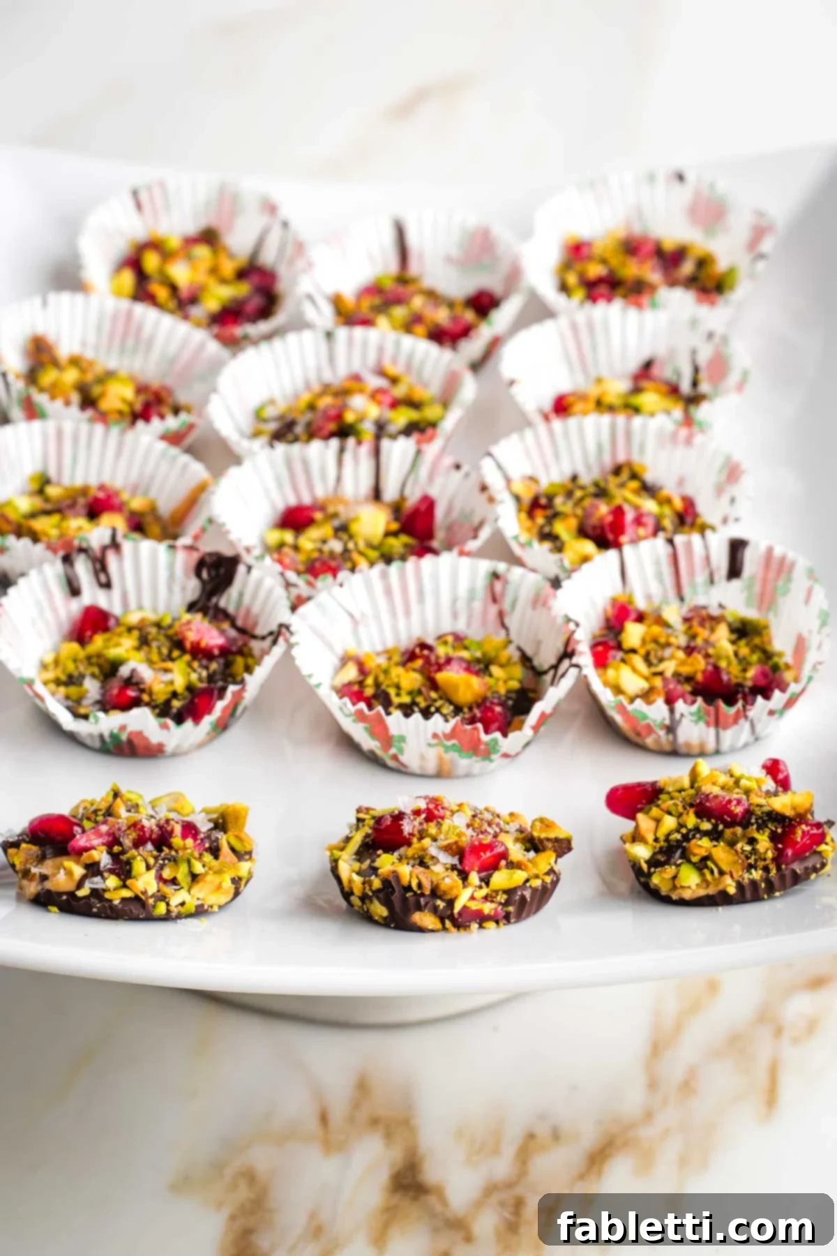 Jeweled Chocolate Peanut Butter Cups 12 Several chocolate peanut butter cups, some unwrapped, showing the layers of chocolate, peanut butter, pistachios, and pomegranate.