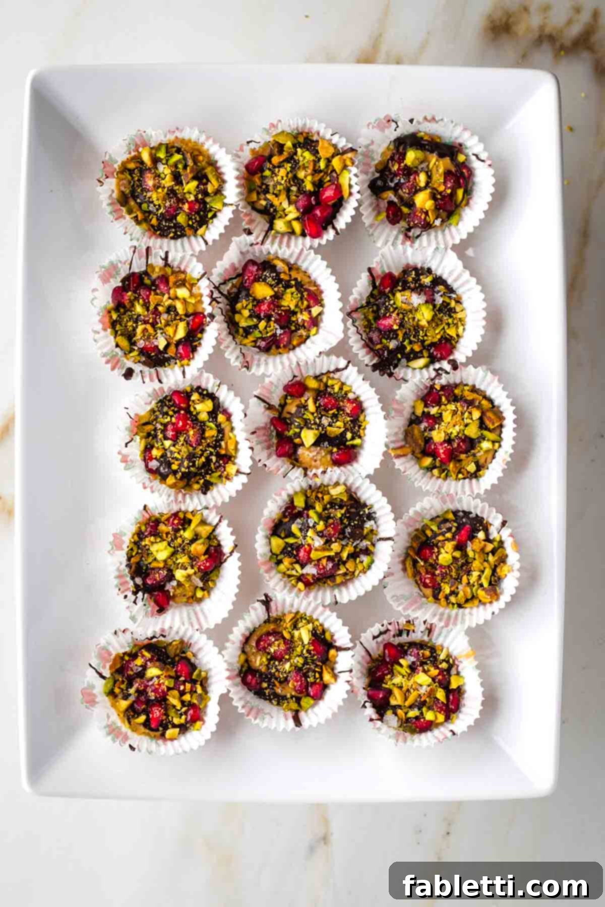 Jeweled Chocolate Peanut Butter Cups 13 A platter generously filled with chocolate peanut butter cups, adorned with pistachios and pomegranate seeds.