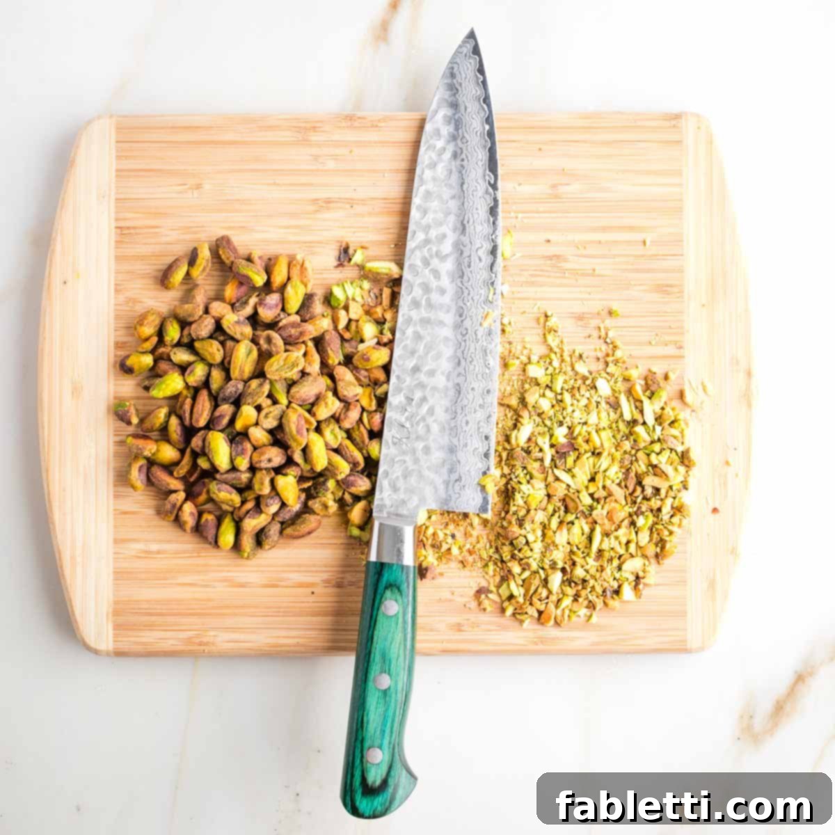 Jeweled Chocolate Peanut Butter Cups 4 Chopping pistachios on a cutting board, with some already finely chopped.
