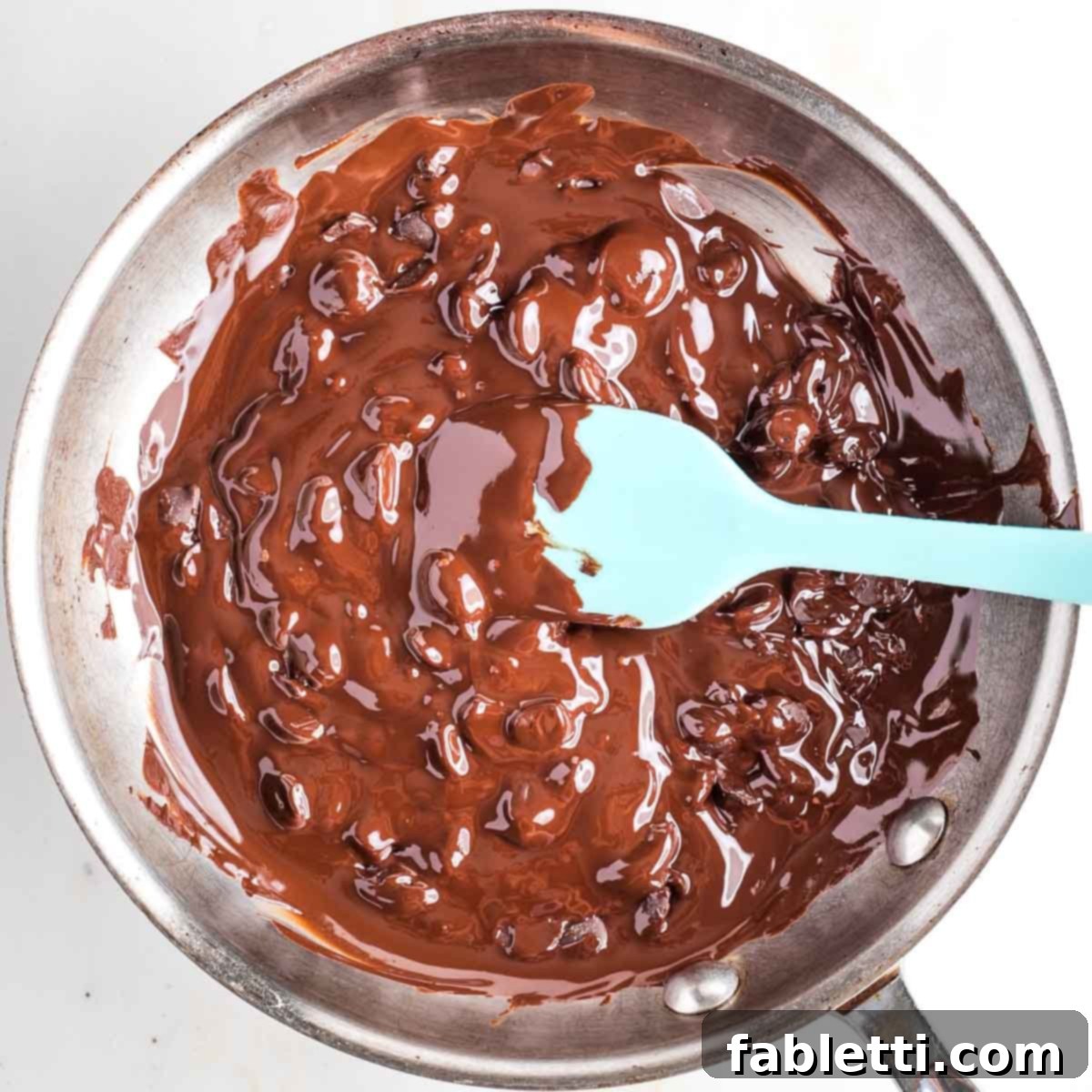 Jeweled Chocolate Peanut Butter Cups 6 Stirring melting chocolate in a skillet with a blue silicone spatula.