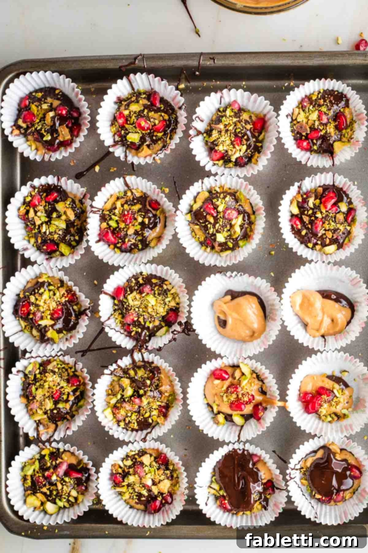 Jeweled Chocolate Peanut Butter Cups 10 A rimmed baking tray filled with mini chocolate peanut butter cups, each topped with nuts and pomegranate.