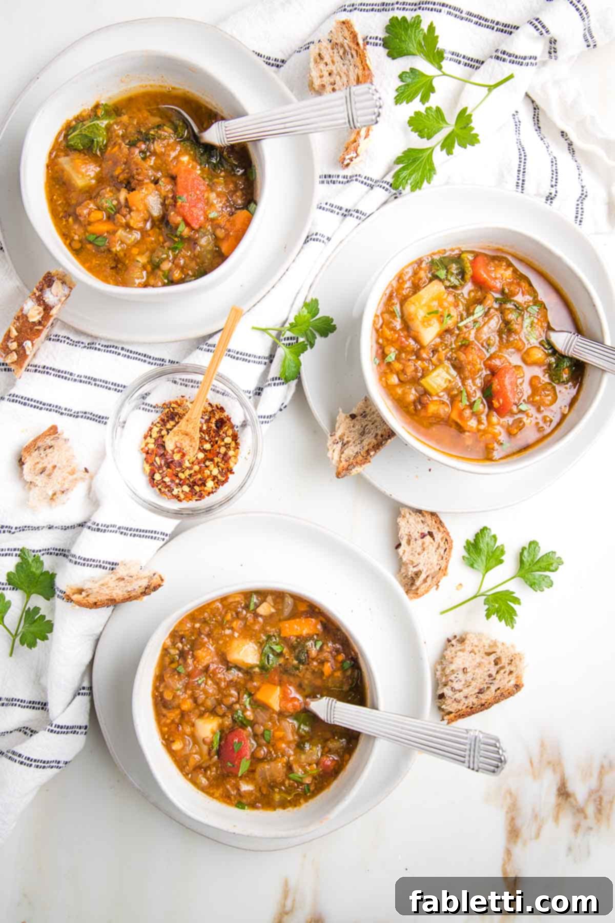 Wholesome Plant-Based Lentil Soup 2 Bowls of chunky lentil soup with crusty bread, fresh parsley and a dish towel.