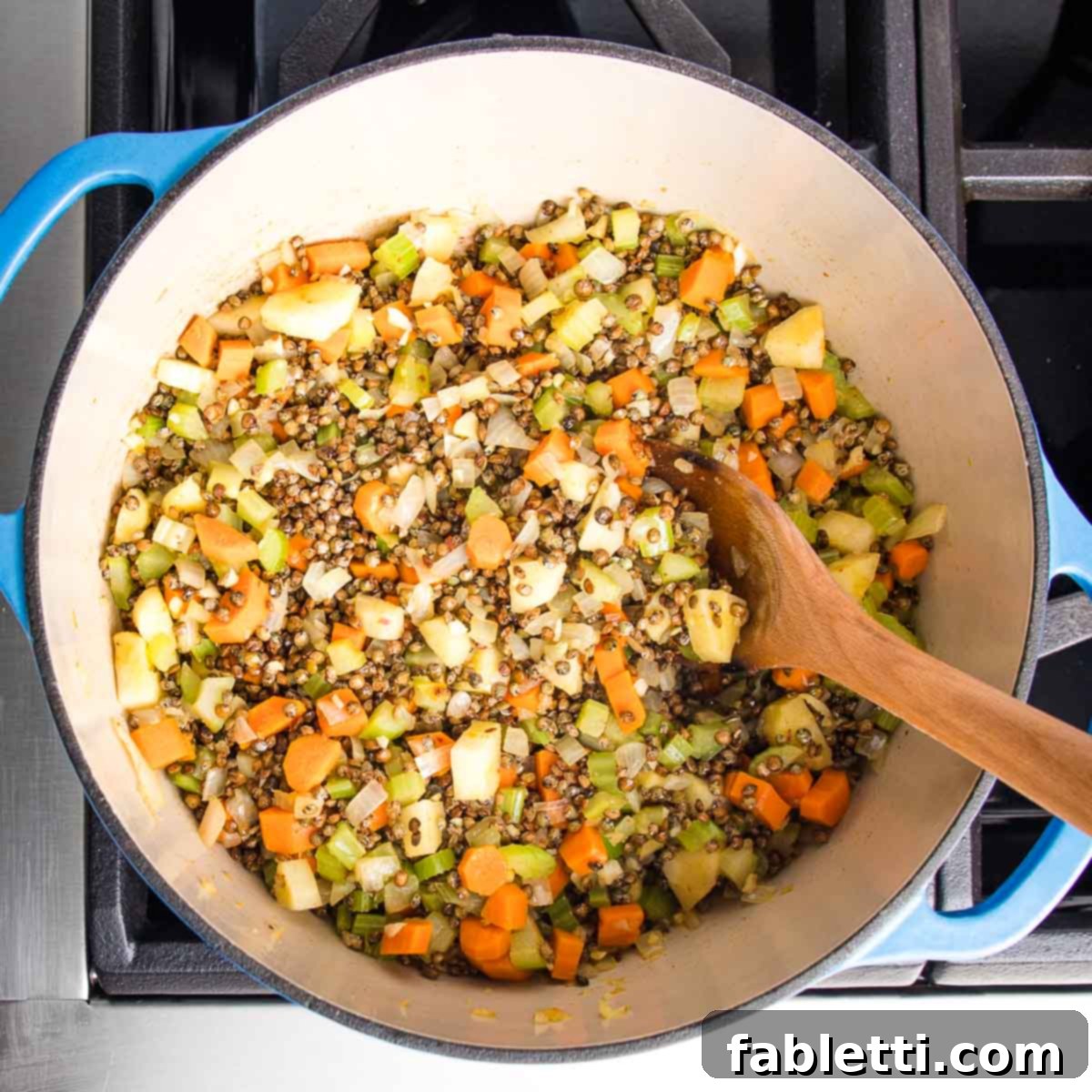 Wholesome Plant-Based Lentil Soup 11 Lentils and chopped veggies in a dutch oven with wooden spoon stirring.