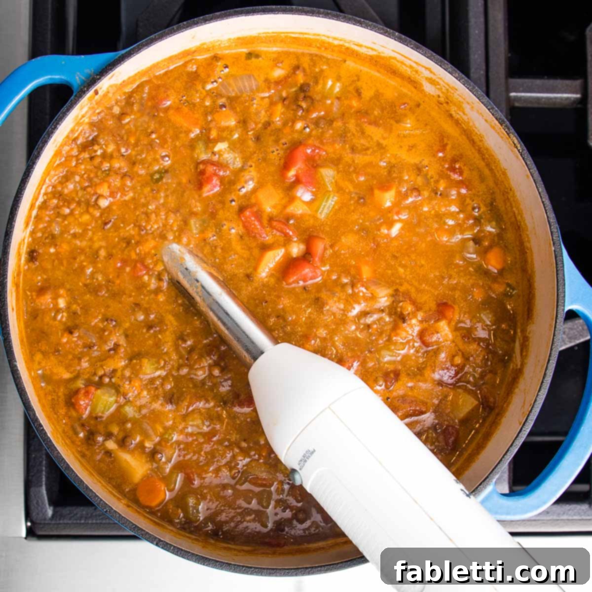 Wholesome Plant-Based Lentil Soup 14 Immersion blender in the center of a dutch oven filled with chunky vegan lentil soup