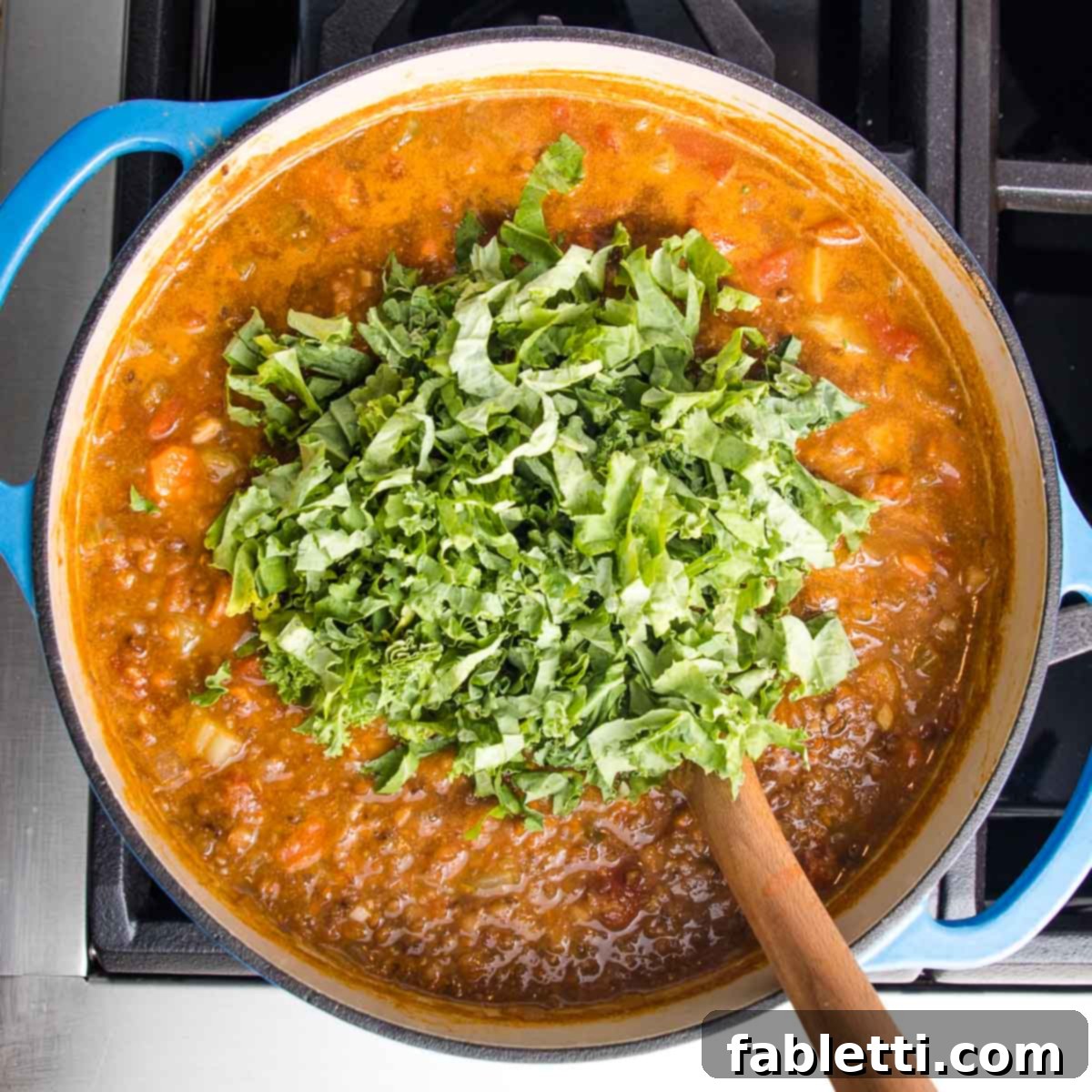 Wholesome Plant-Based Lentil Soup 16 Dutch oven filled with lentil soup and a large pile of kale on top.