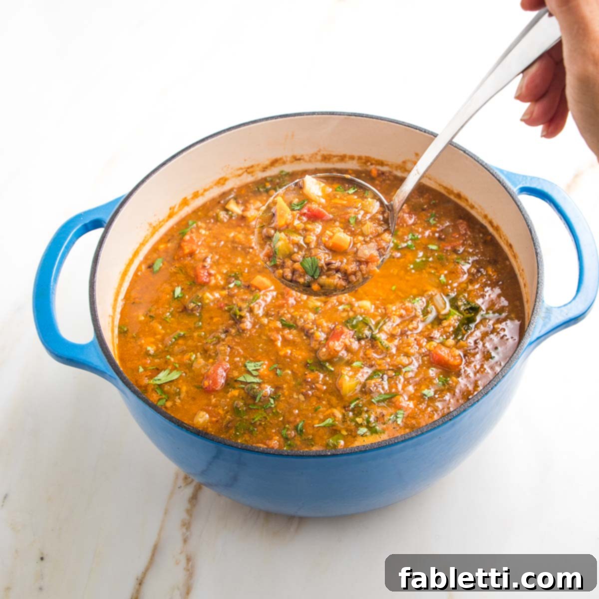 Wholesome Plant-Based Lentil Soup 18 Blue dutch oven filled with chunky lentil soup. A ladle full is shown close up.