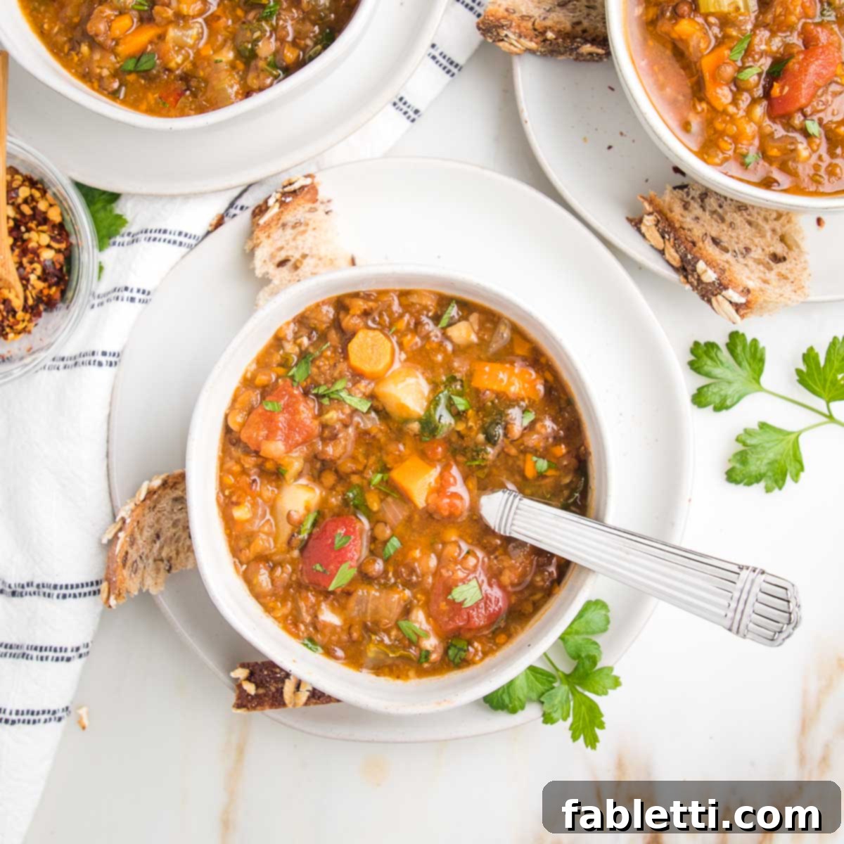 Wholesome Plant-Based Lentil Soup 3 Chunky vegetable lentil soup in bowls with crusty bread pieces on the side.