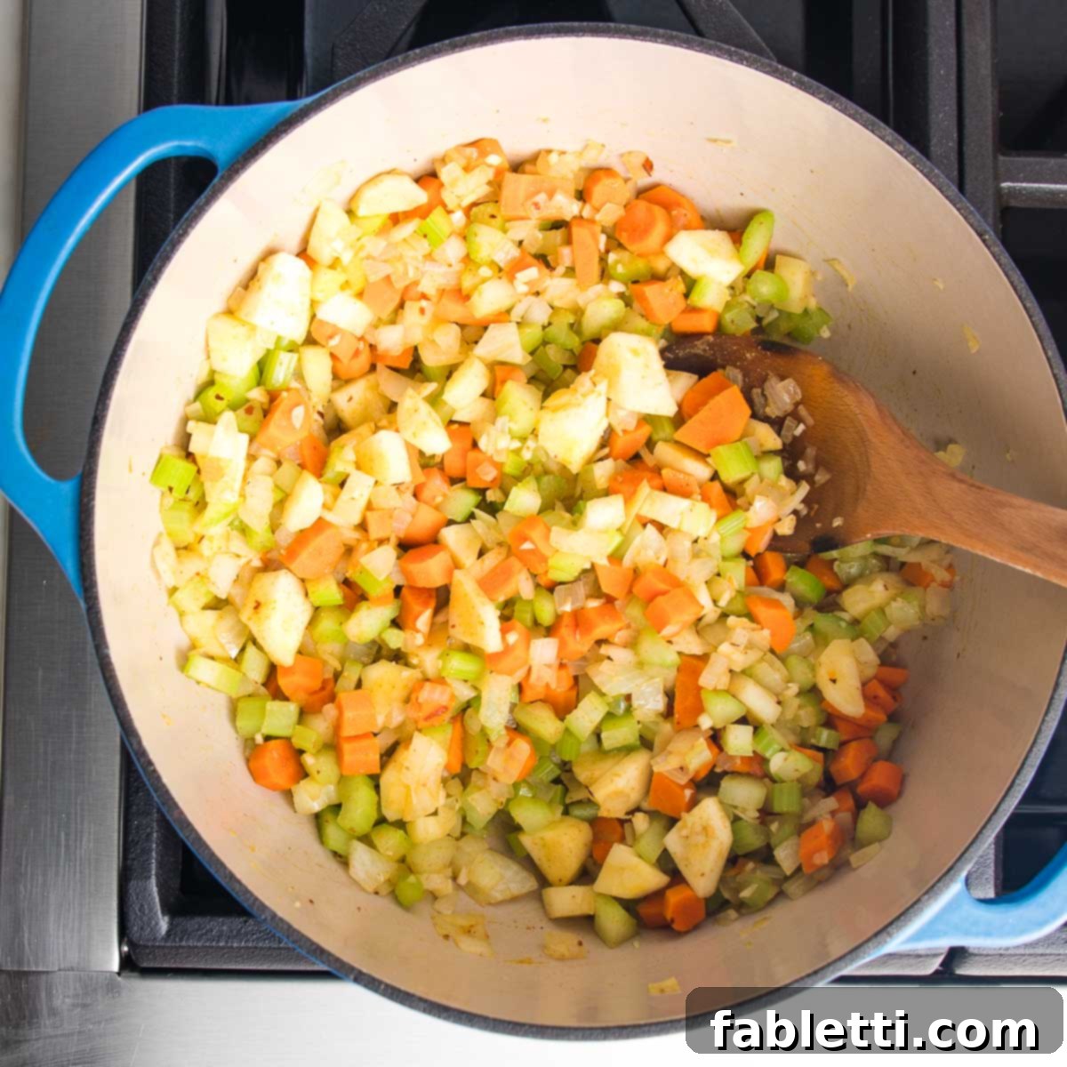 Wholesome Plant-Based Lentil Soup 9 Dutch oven filled with chopped carrots, parsnips, celery and onions, stirred with a wooden spoon.