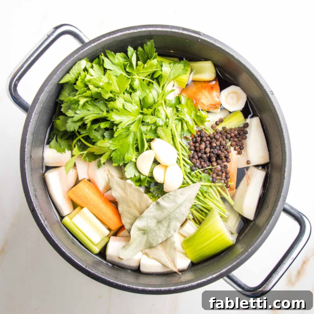 Stock pot with carrots, celery, parsley, parsnips peppercorns floating on top.