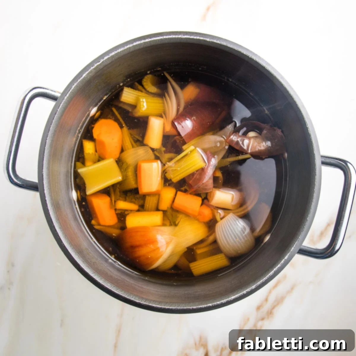 Cooked vegetables in a large pot filled with water that is now broth.