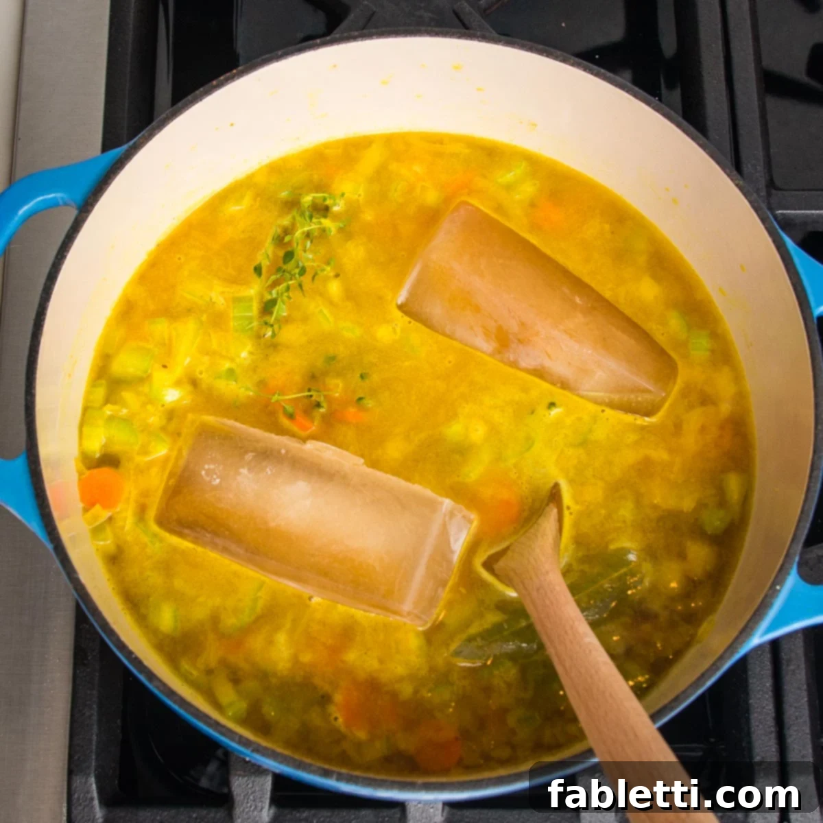 Dutch oven with soup cooking and a couple large cubes of veggie broth melting into the pot of soup.