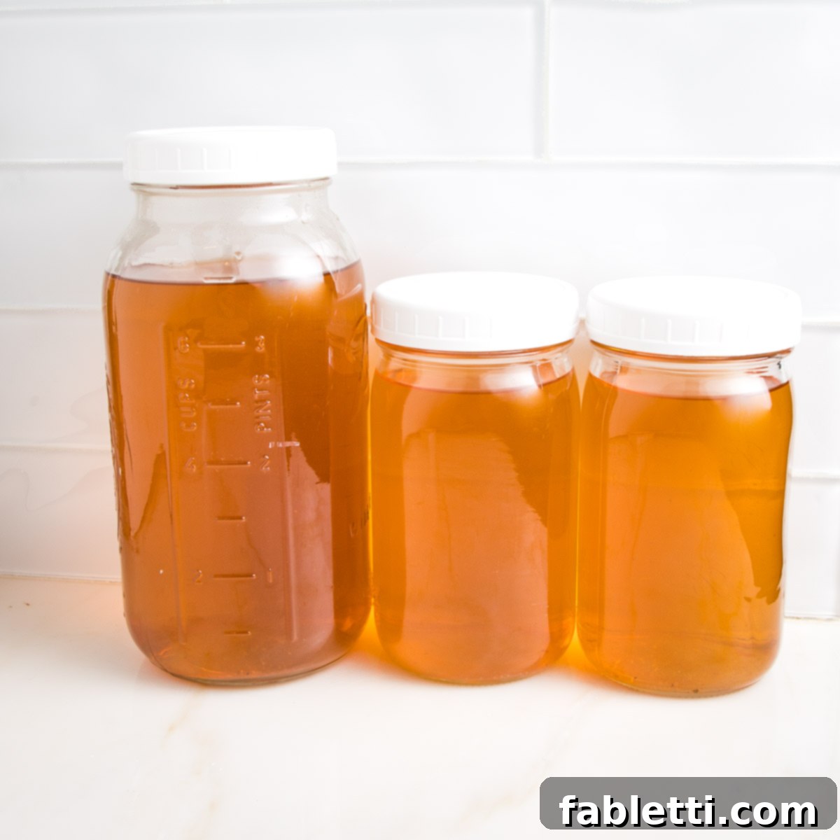 Three glass mason jars with white plastic tops. All are filled with golden colored liquid...homemade vegetable broth.