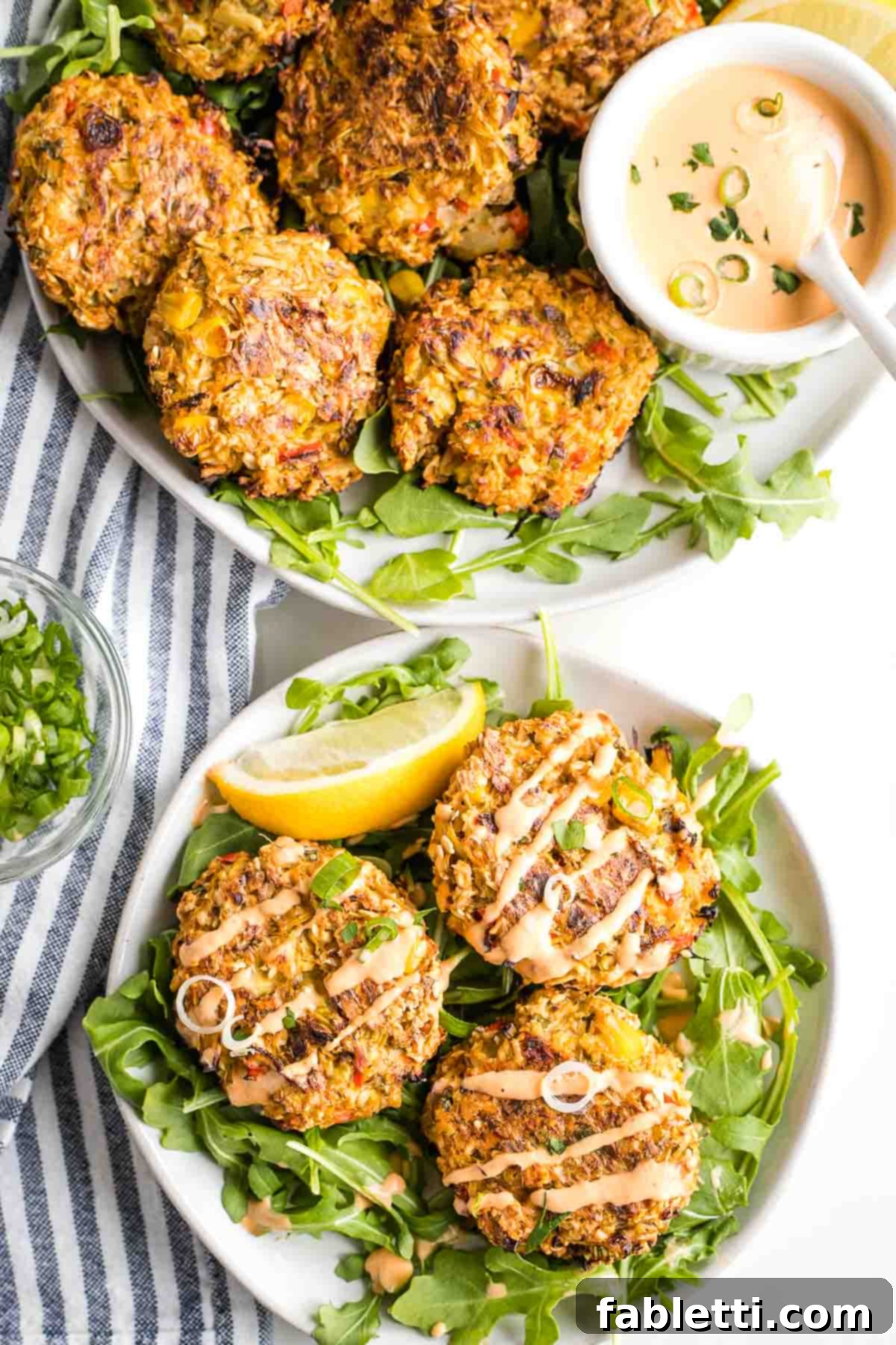 Vegan crab cakes on a platter with sriracha dipping sauce, plus a small plate with arugula and crab cakes. 