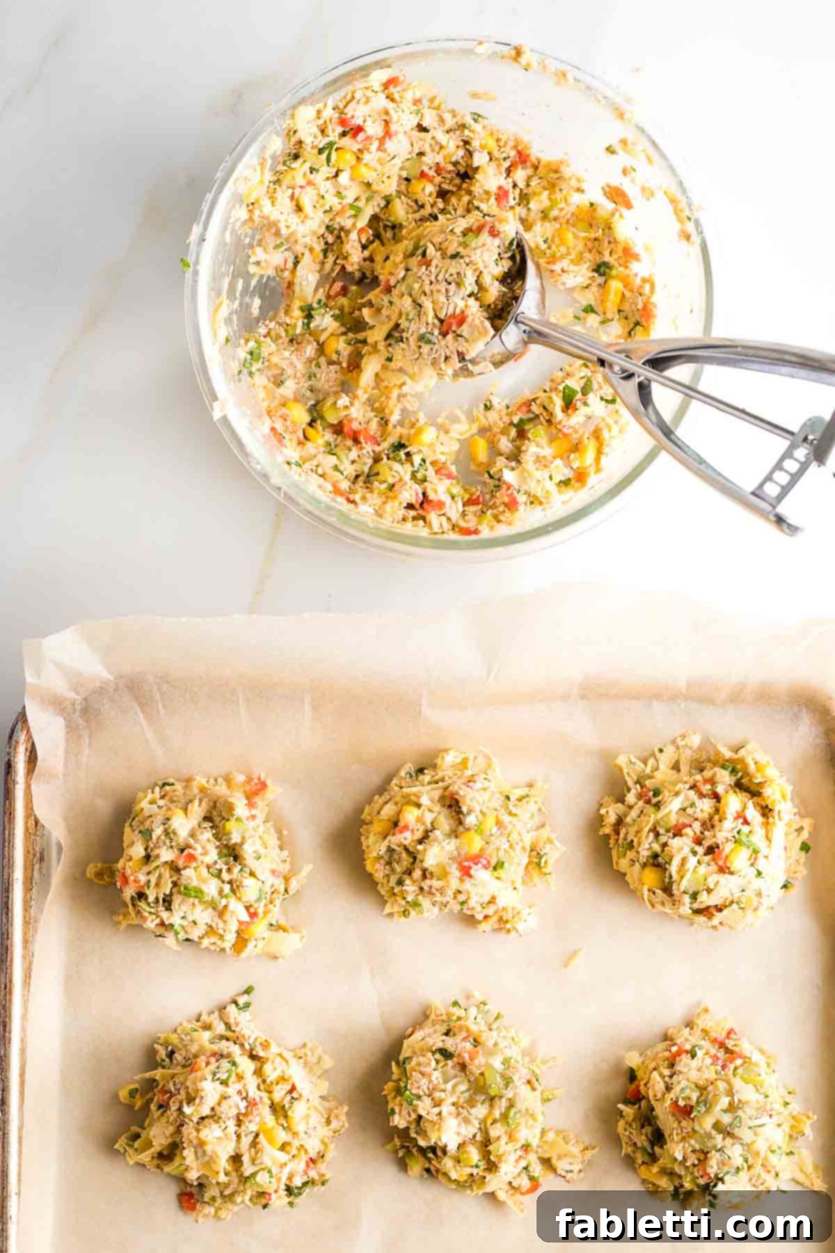 Scooping artichoke crab cakes onto baking tray lined with parchment paper.