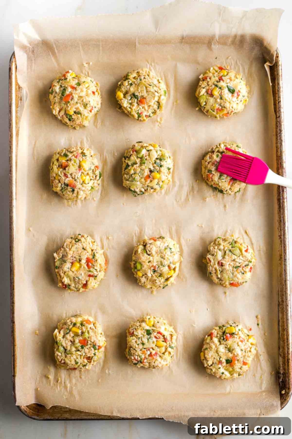 Brushing oil onto vegan artichoke cakes on a baking sheet.
