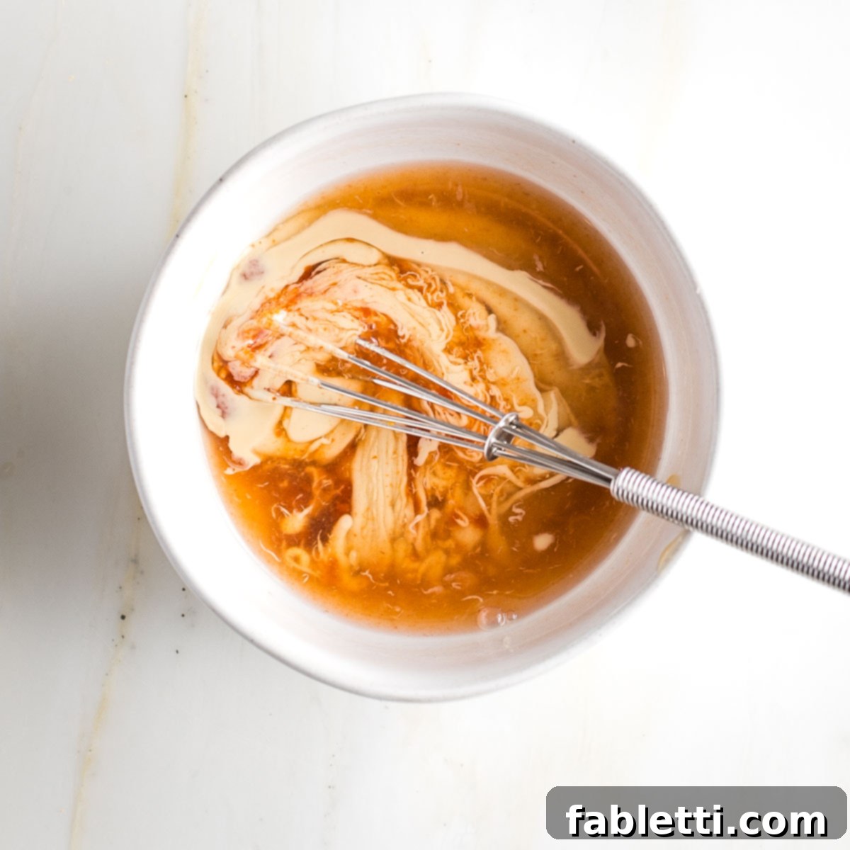 Whisking together tahini, sriracha, lemon juice and pickle juice in a small bowl.. 