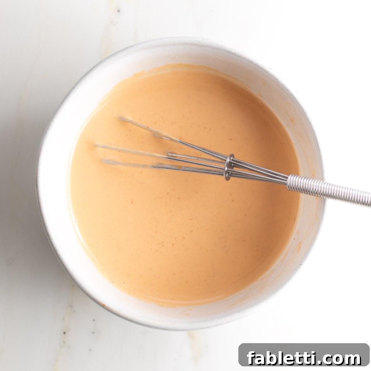 Whisk in a small bowl full of light orange sauce.