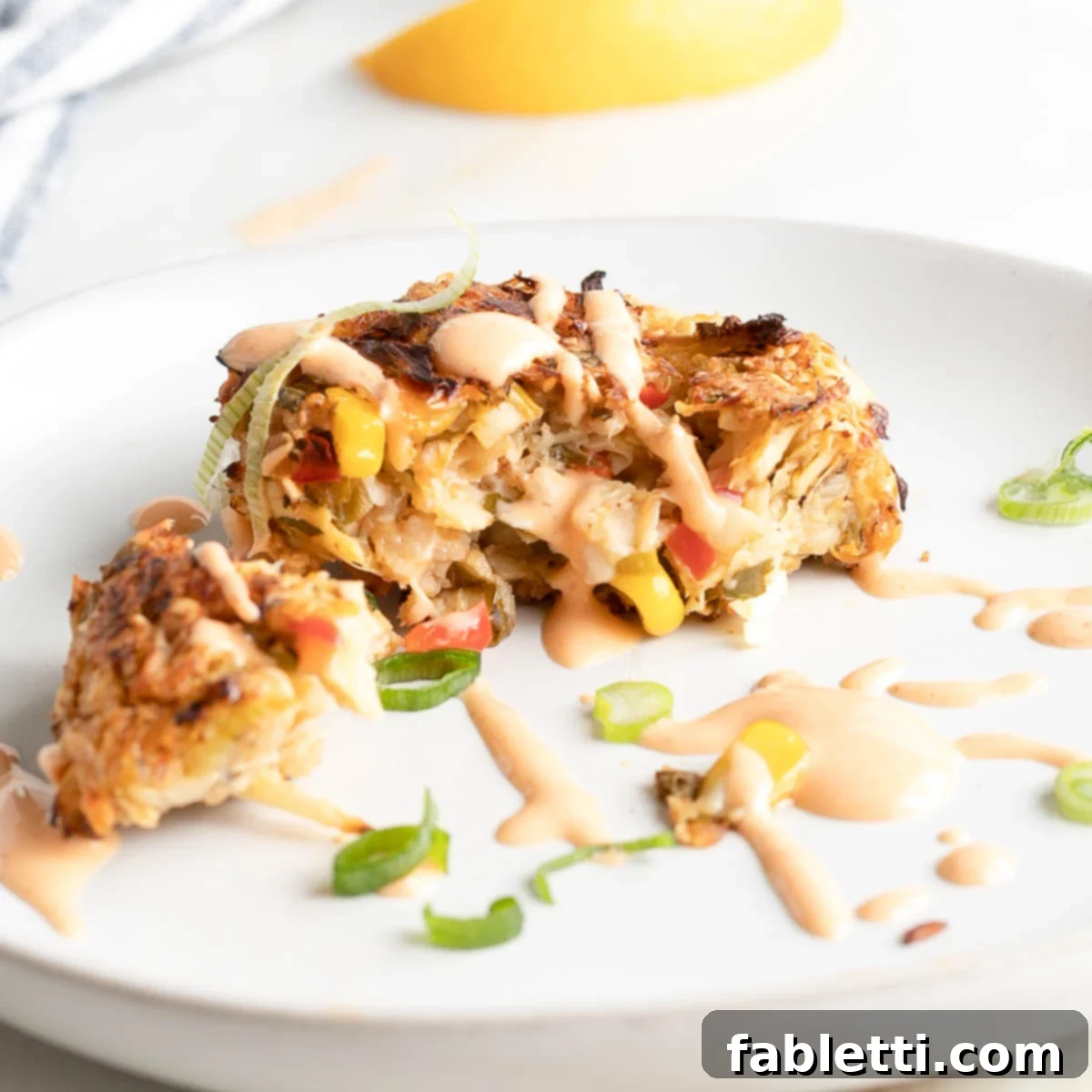 Vegan crab cake cut open to show texture, plus some drizzled sriracha sauce dripping down.