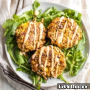 Three vegan crab cakes set atop arugula and drizzled with sriracha tahini.