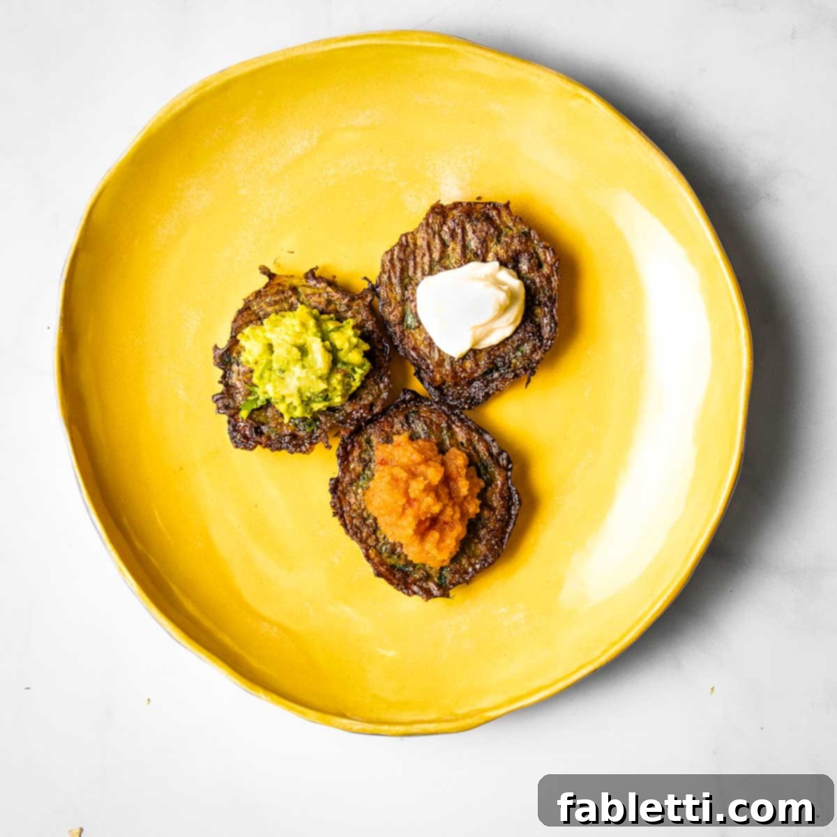 Oven-Baked Crispy Brussels Sprout Latkes 2 Three golden brown Brussels sprouts latkes with vibrant toppings: classic applesauce, creamy guacamole, and tangy sour cream.