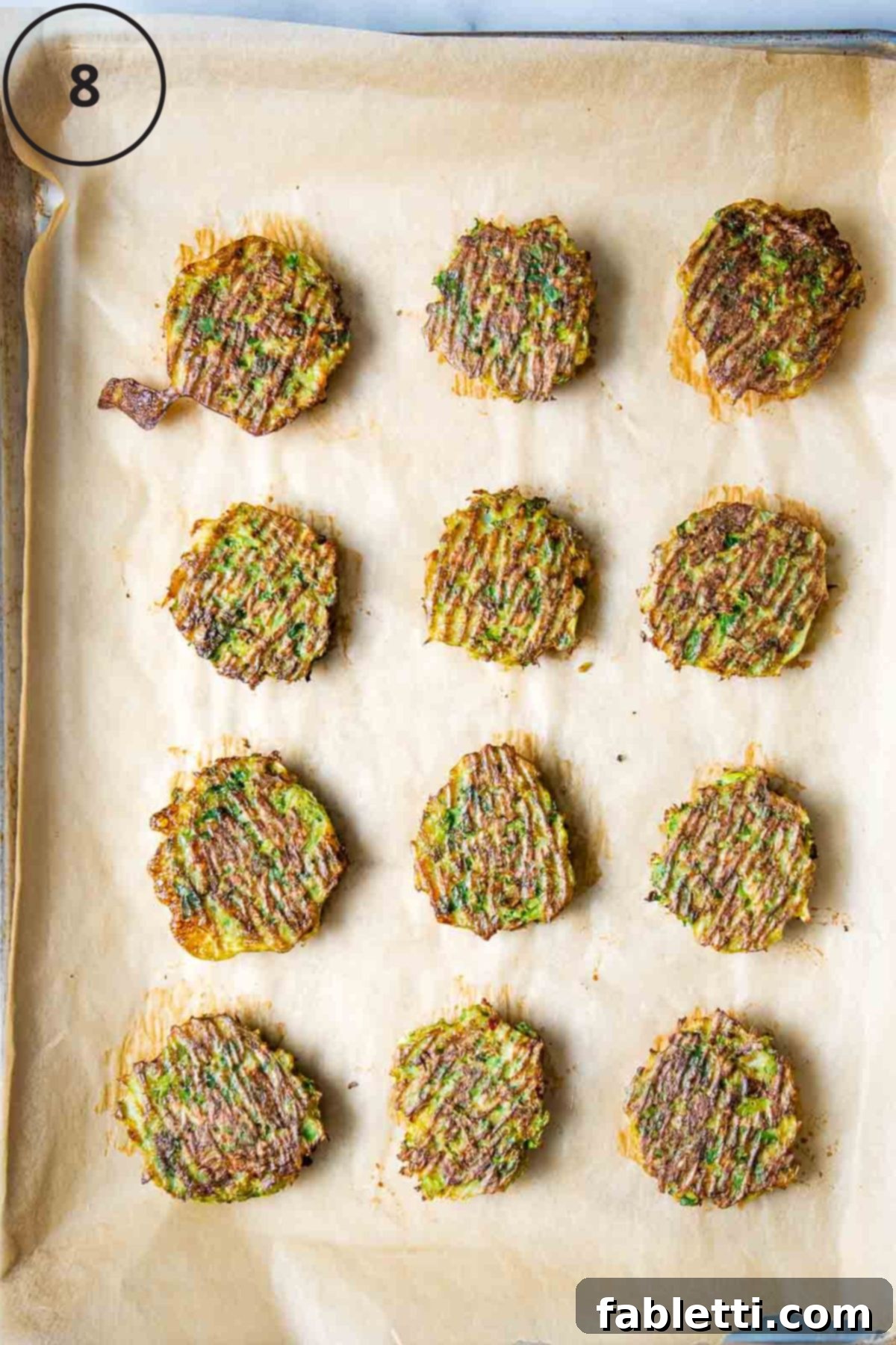 Oven-Baked Crispy Brussels Sprout Latkes 11 Golden-brown and crispy Brussels sprouts latkes, freshly baked and arranged perfectly on a parchment-lined baking sheet, ready to be served.