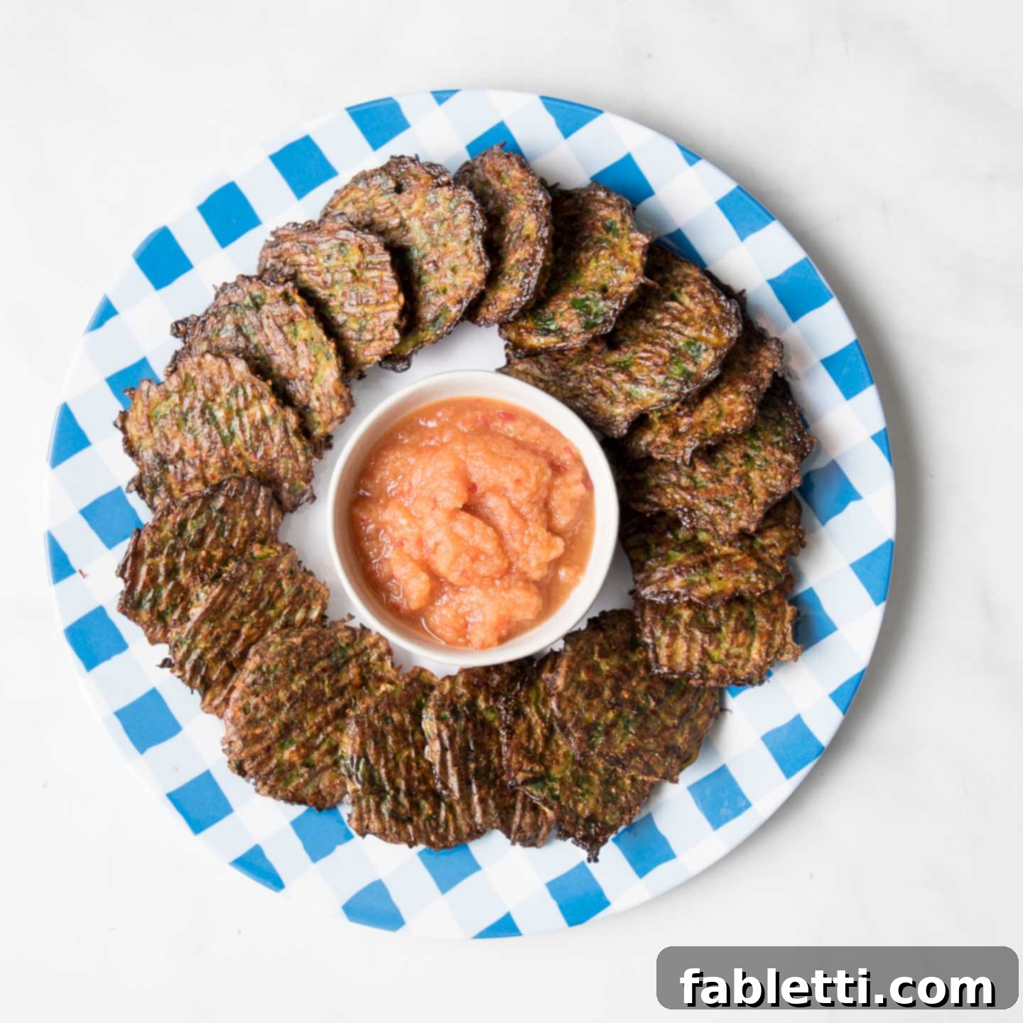 Oven-Baked Crispy Brussels Sprout Latkes 12 A plate of golden Brussels sprouts latkes elegantly paired with a small dish of vibrant pink applesauce, ready for serving.